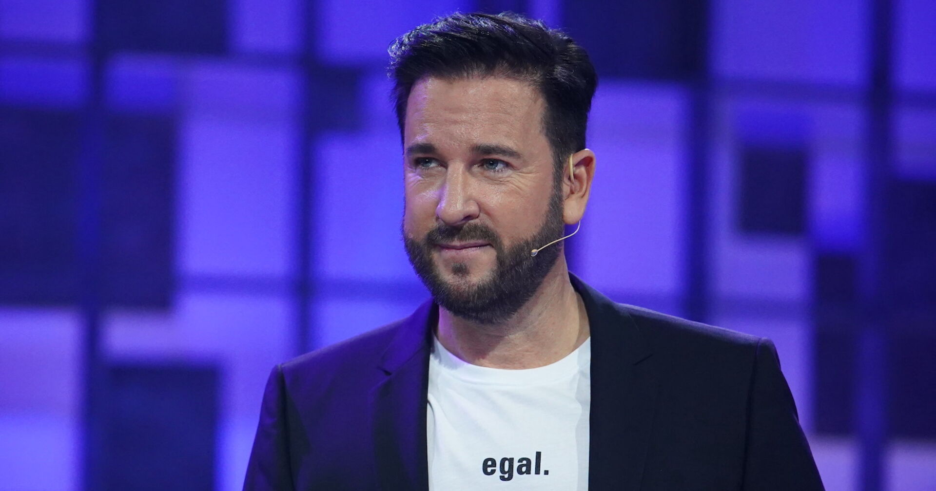 Michael Wendler in einem schwarzen Sakko mit einem weißen T-Shirt auf dem "egal." steht.