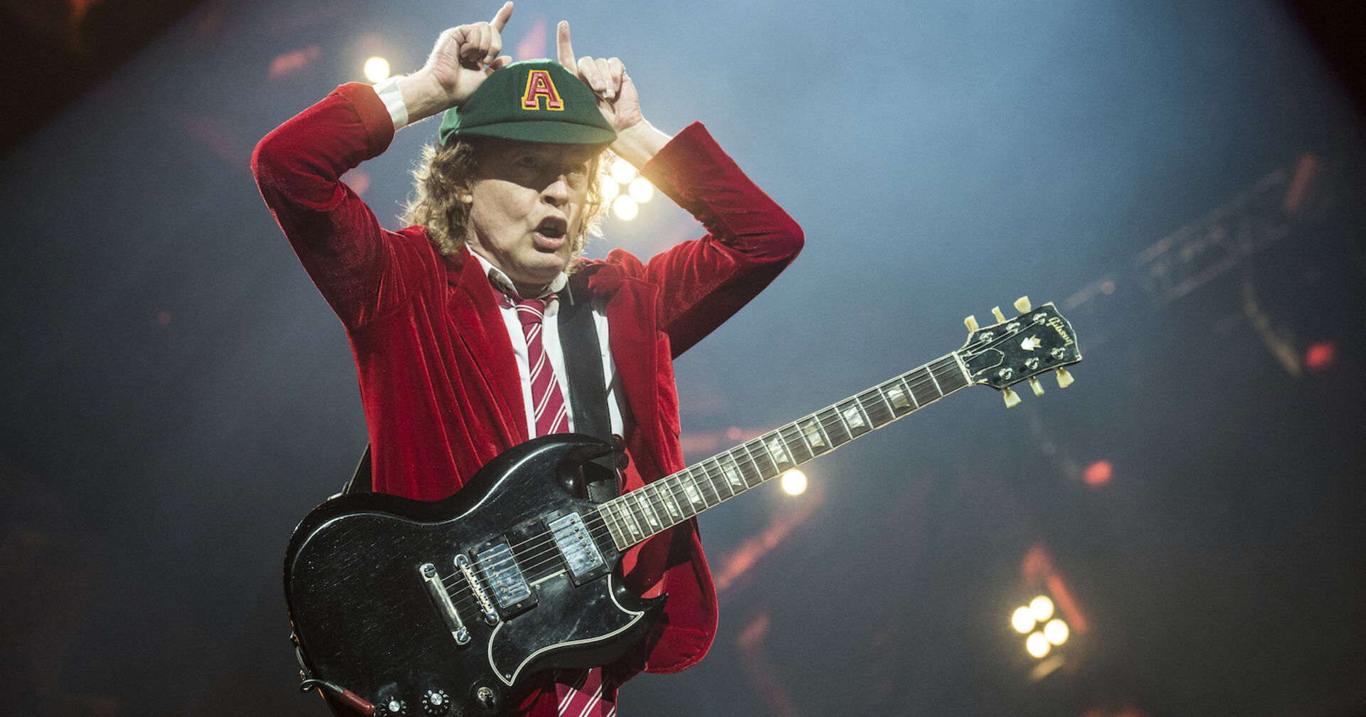 AC/DC Gitarrist Angus Young mit einem roten Blazer und einer Kappe auf der Bühne.