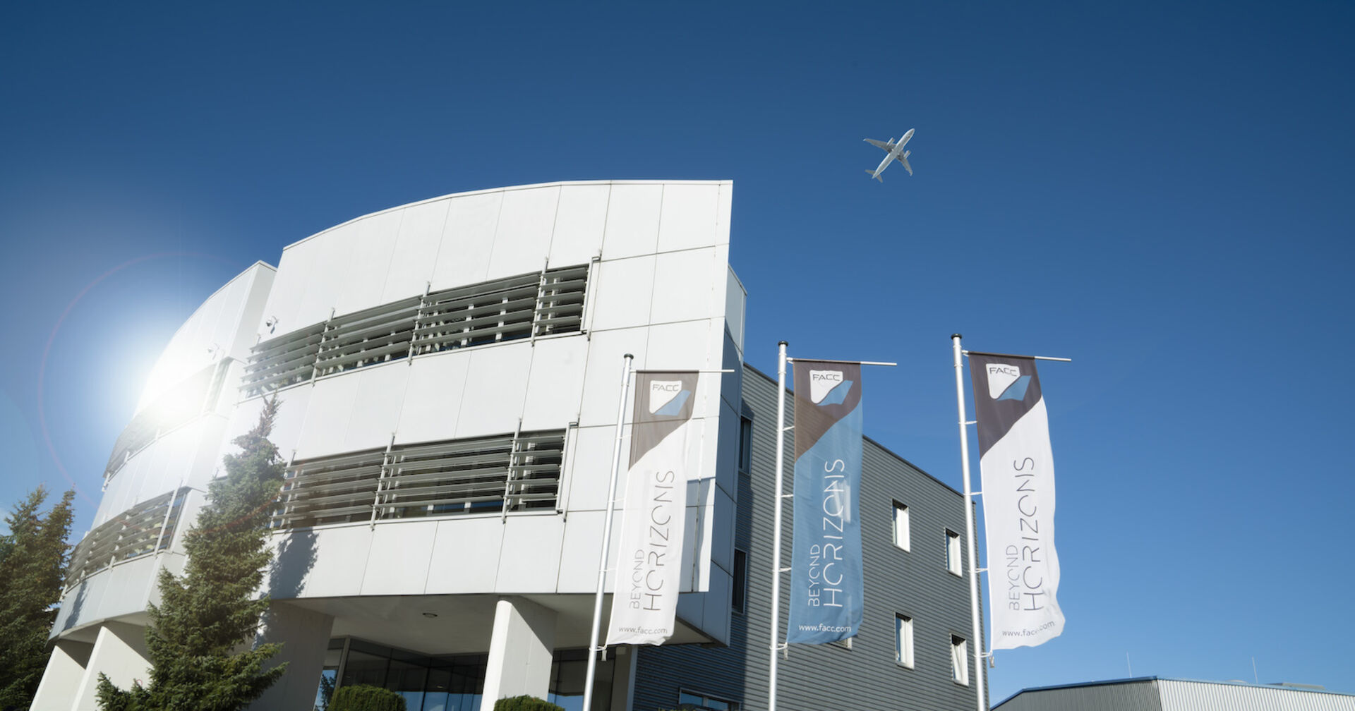 Flugzeug fliegt über ein weißes Bürogebäude | Credit: FACC/Gortana