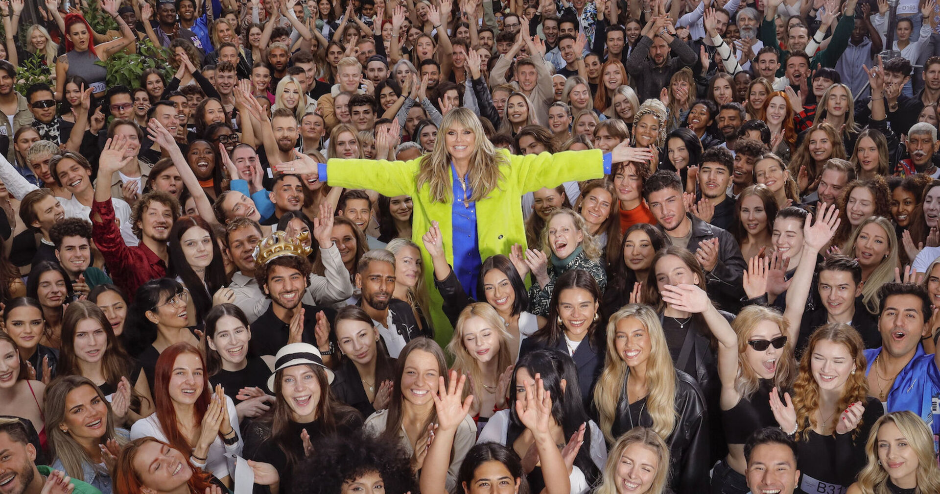 Heidi Klum mit einer gelben Jacke inmitten von Teilnehmern für Germanys Next Top Model 2024 bei einem Casting.