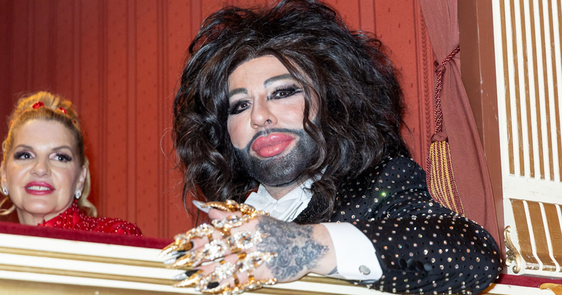 Harald Glööckler mit viel goldenen Schmuck und langen schwarzen Haaren auf dem Opernball 2024.