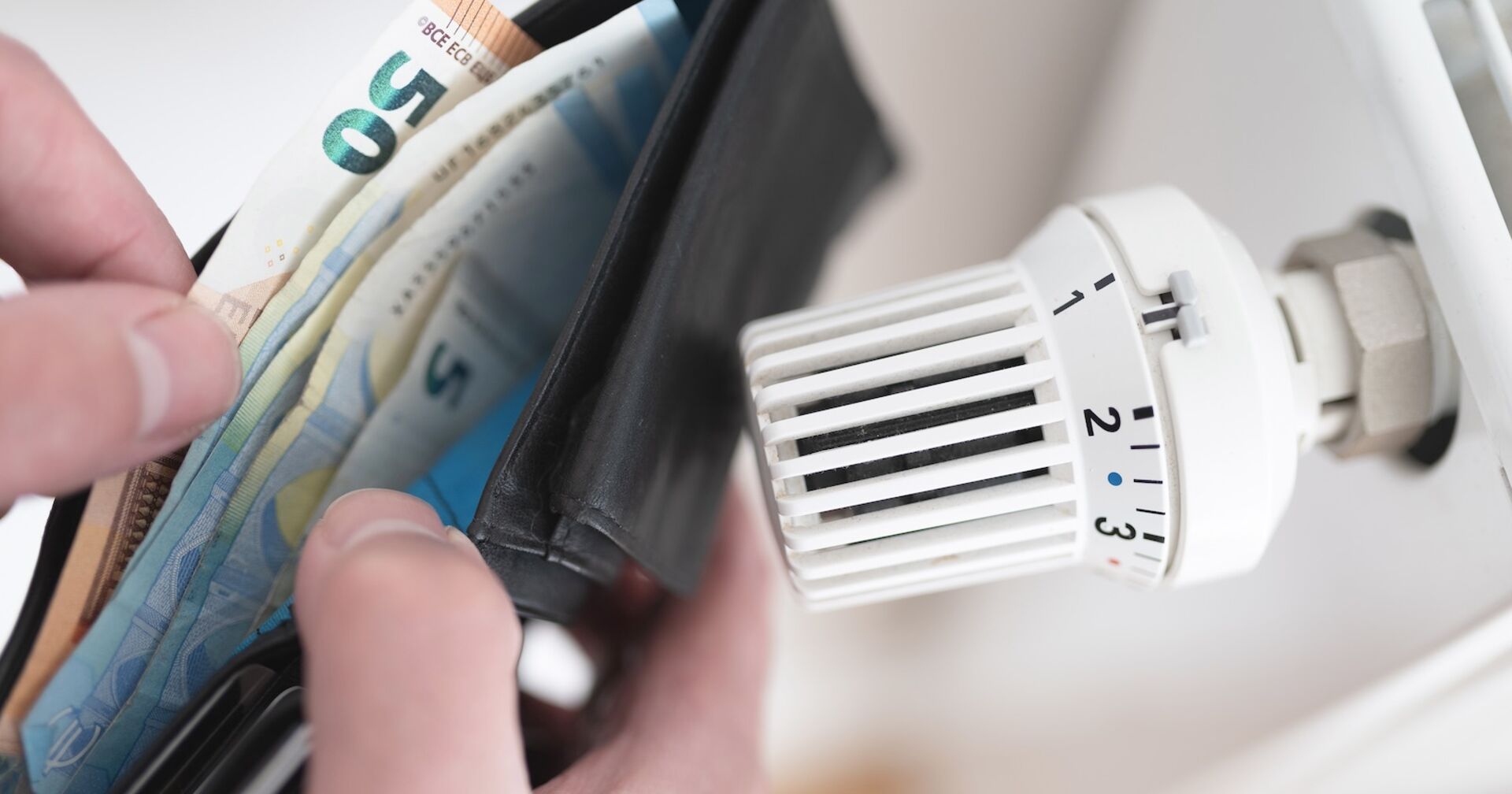 Jemand schaut über einer Heizung in seine Geldtasche.