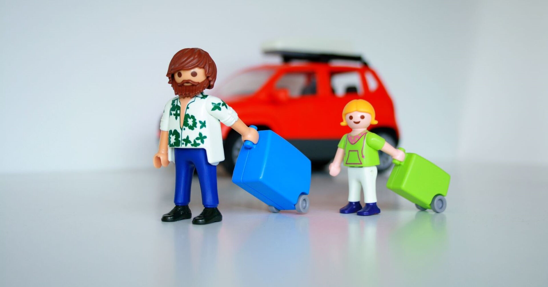 Zwei Playmobilfiguren, ein Vater und sein Kind mit Koffer in der Hand, im Hintergrund ein rotes Auto