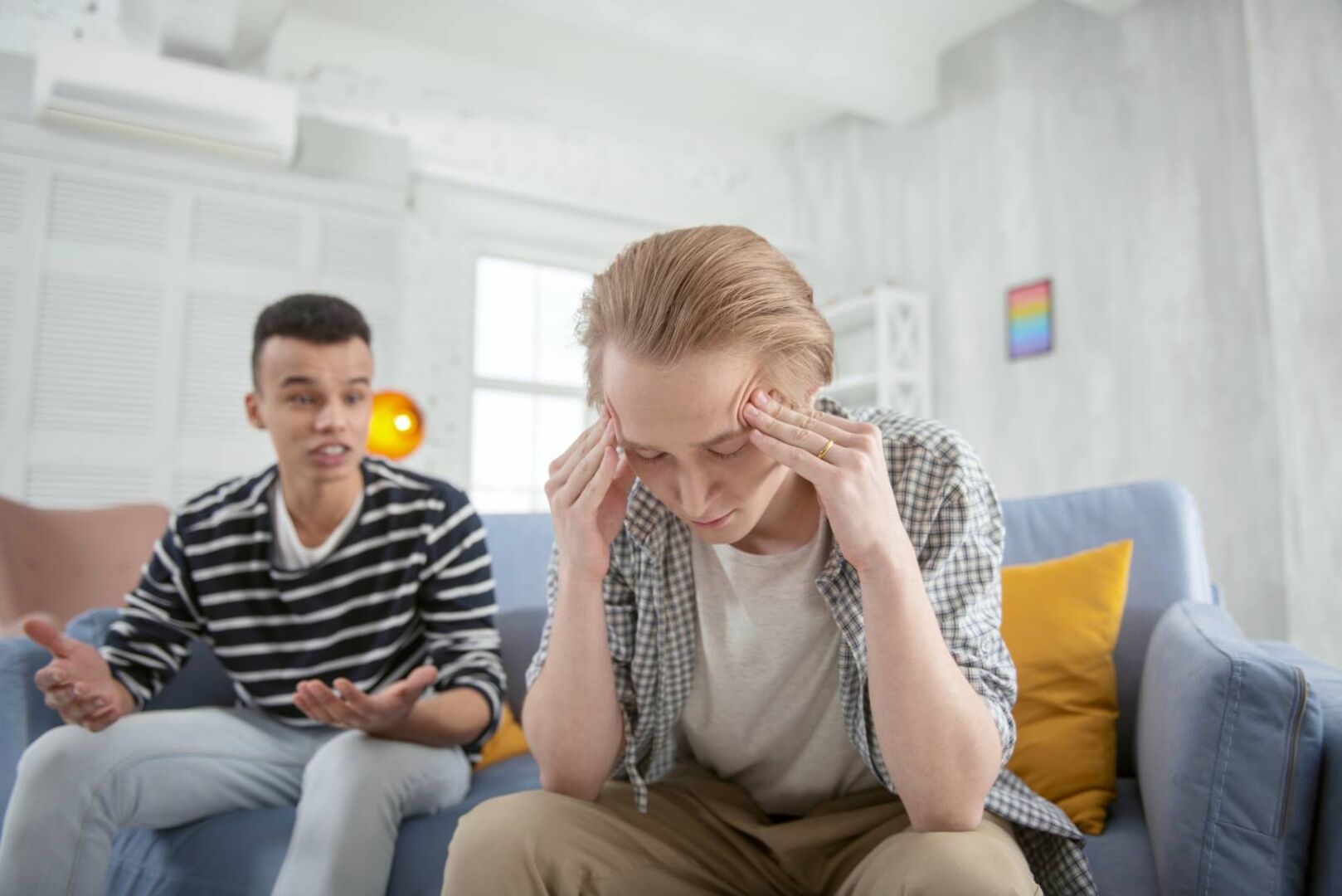 Junges Paar sitzt auf dem Sofa, der rechte der beiden hat die Hände vor Verzweiflung an die Schläfen gelegt.