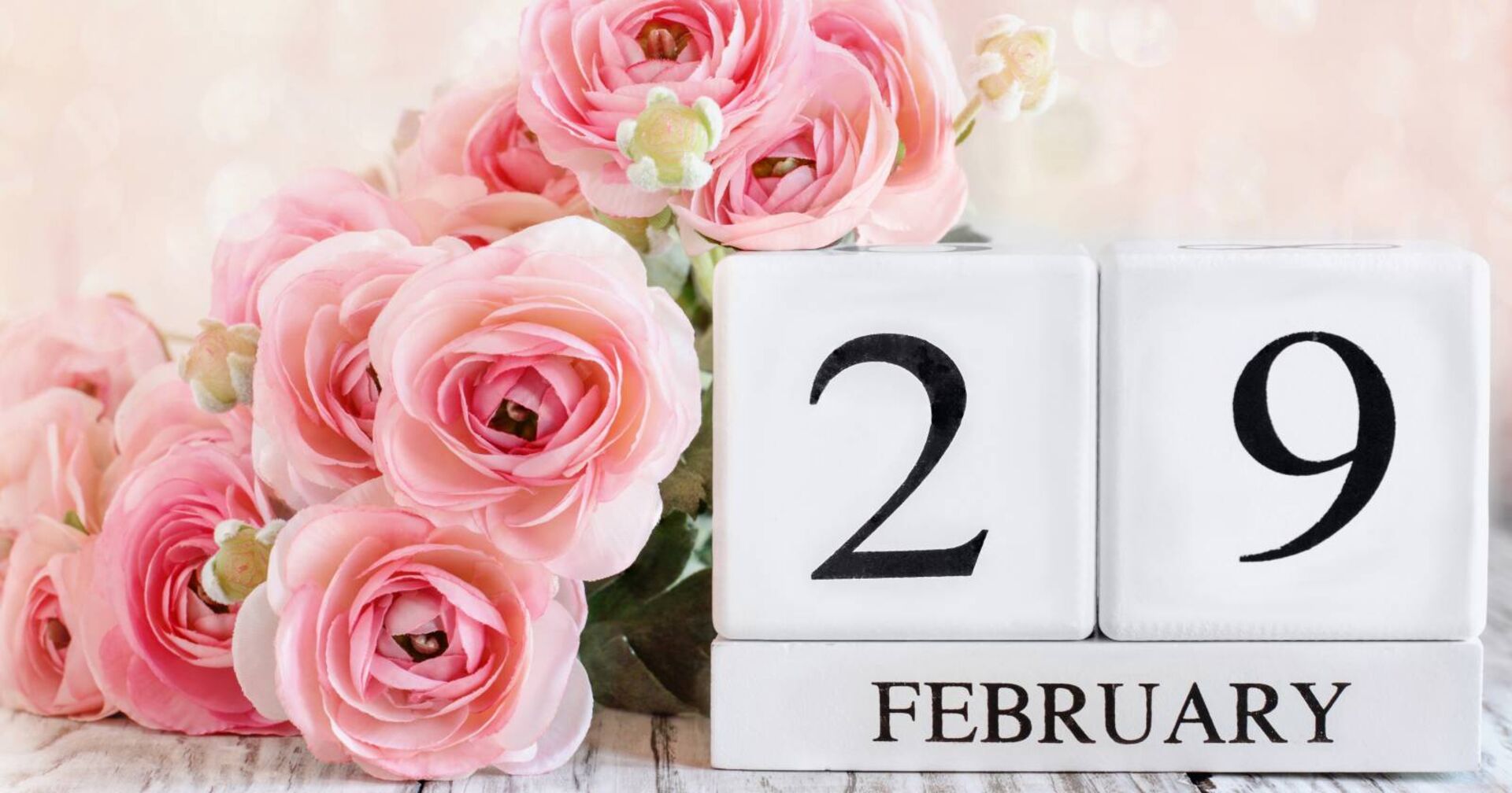 Übereinander gestapelte weiße Holzklötze, die zusammengesetzt den "29. Februar" ergeben, verziert mit rosa Rosen.