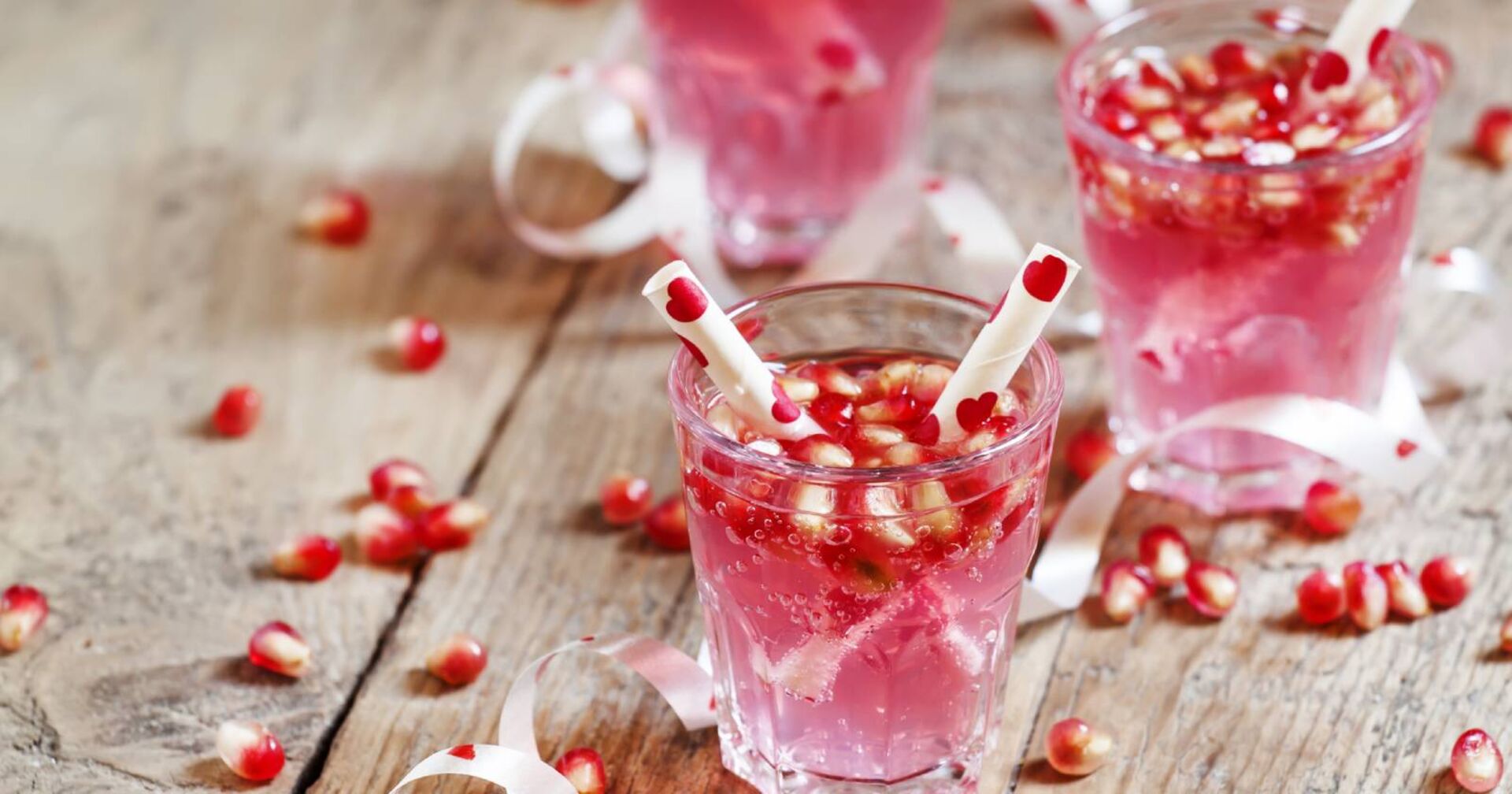 Rosafarbene Cocktails für den Valentinstag, verziert mit Granatapfelkernen und herzförmigen Zuckerstangen