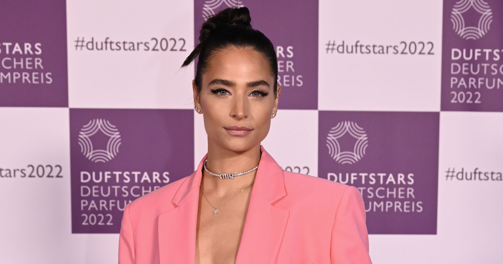 Amira Pocher mit geschlossenen schwarzen Haaren und einem rosa Outfit.