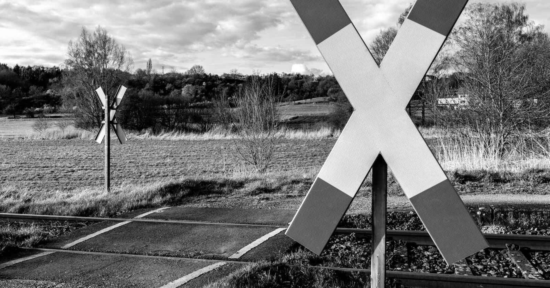 Ein düsteres Schwarz-weiß-Bild von einem Bahnübergang mit Andreaskreuz.
