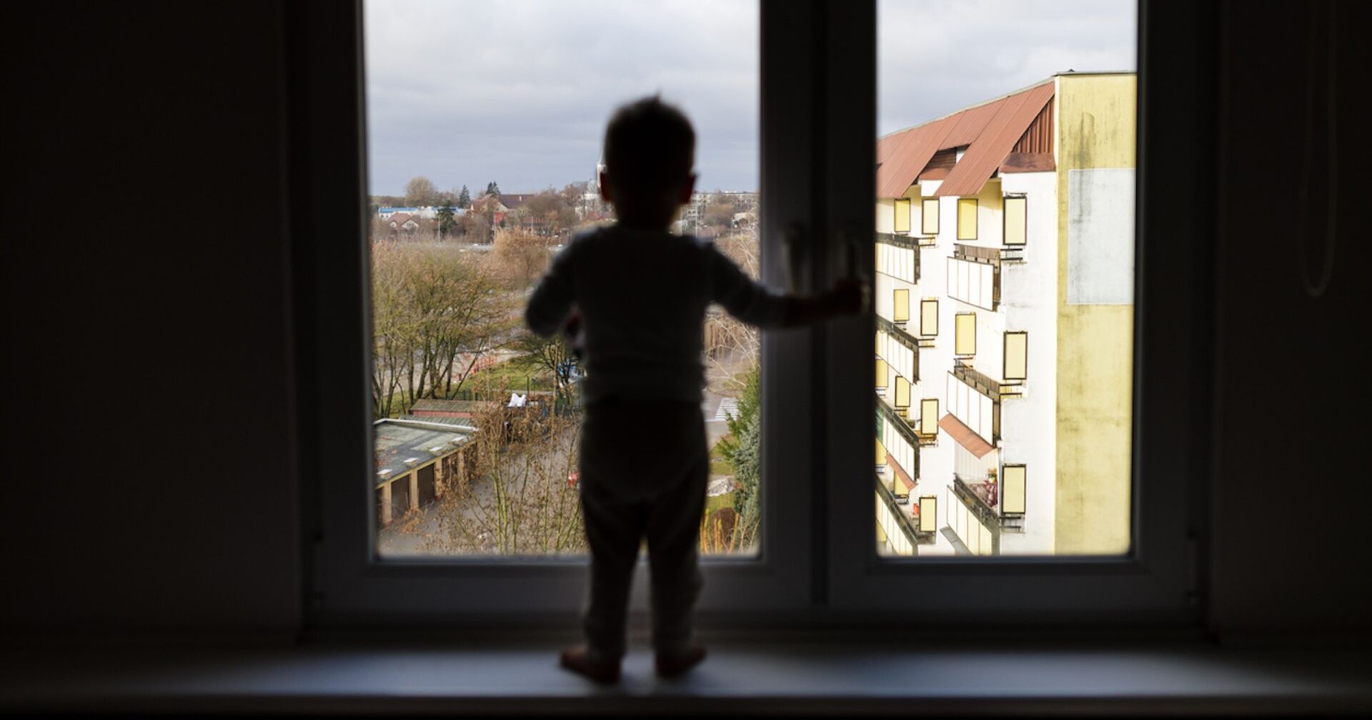 Eine kleiner Bub steht an einem Fenster und möchte es öffnen.
