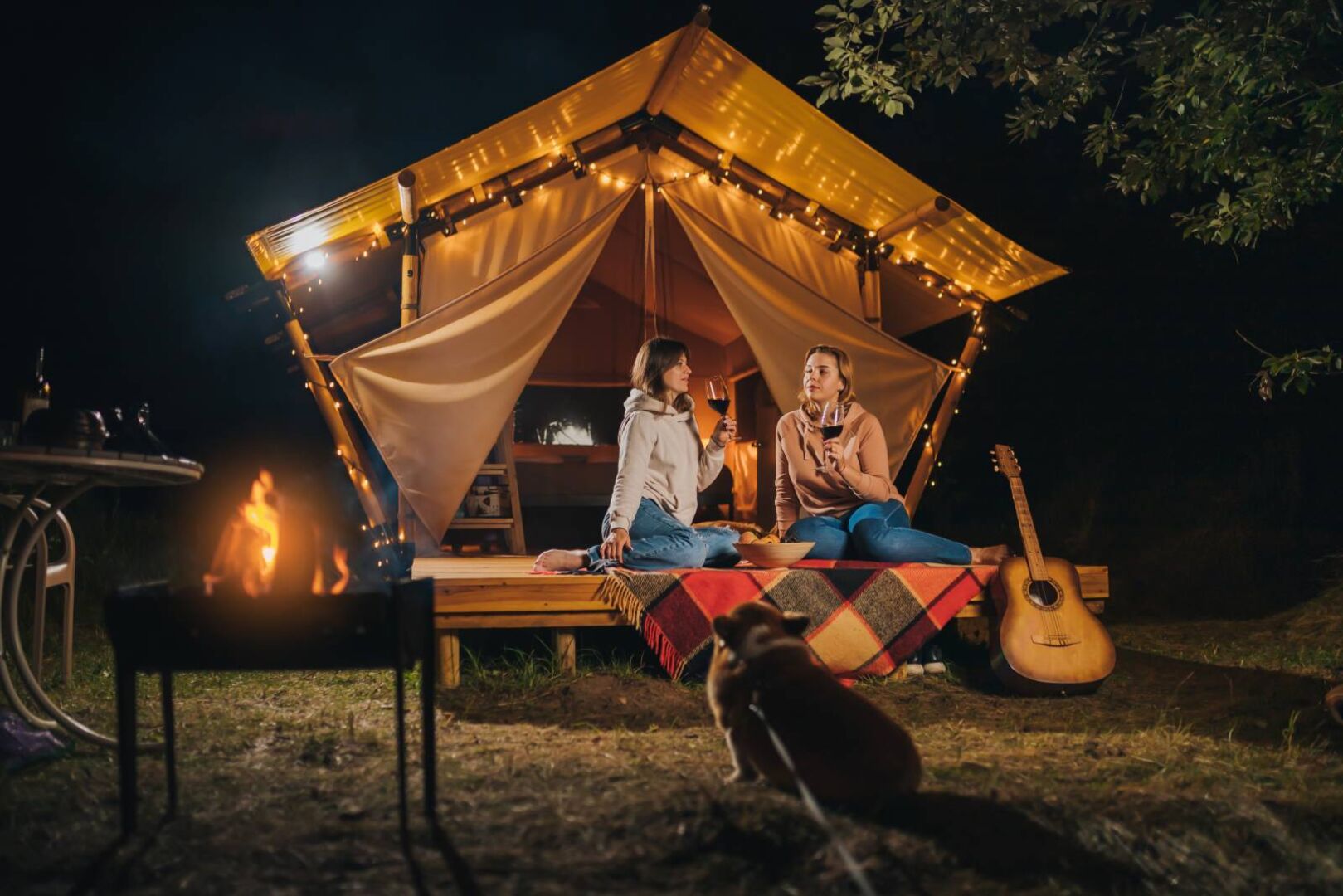 2 Frauen sitzen abends auf der Veranda eines Glamping-Zeltes und trinken gemeinsam Wein.