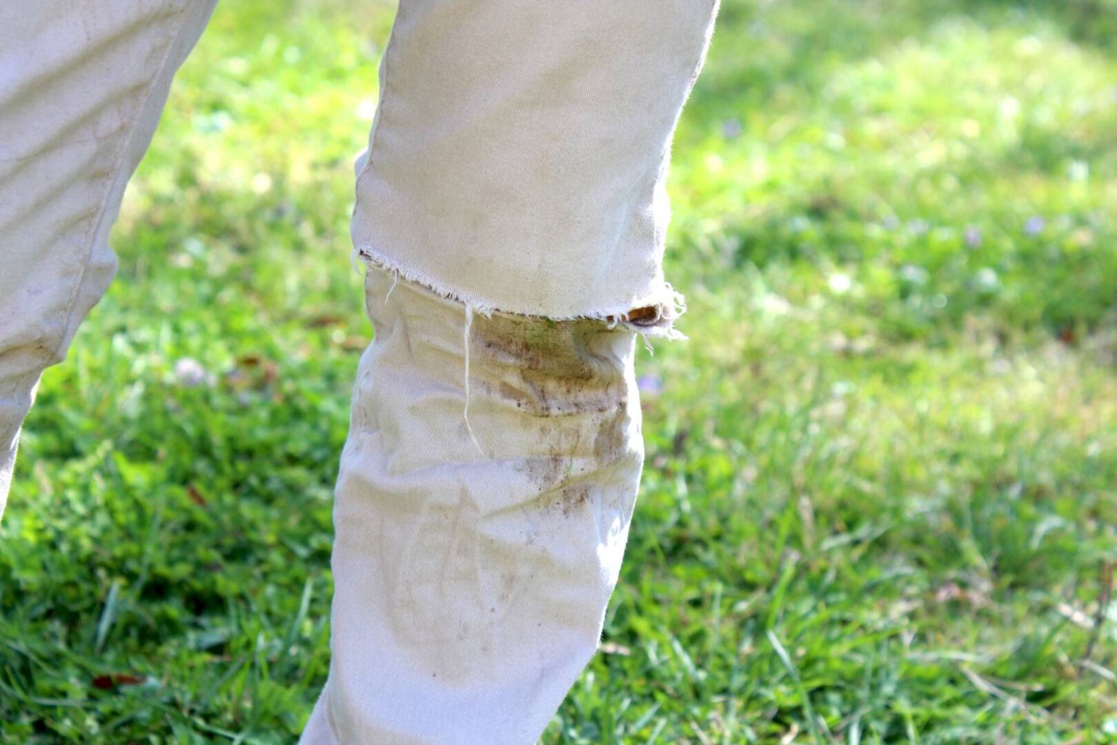 Ausschnitt einer weißen Hose mit einem eingetrockneten Grasfleck auf der Position des Knies.