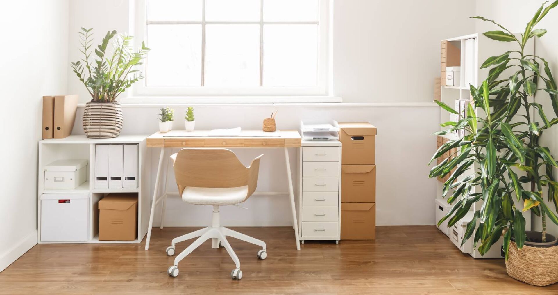 Arbeitszimmer mit weißen Mobilar an Schreibtisch, Drehsessel und Zimmerpflanzen bei hellem Tageslicht.