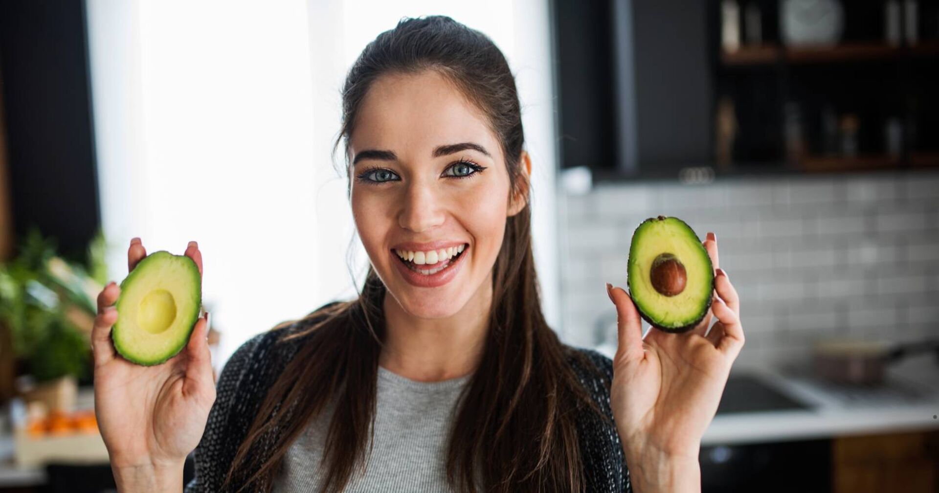 Eine hübsche Frau posiert mit je einer aufgeschnittenen Avocadohälfte, die sie lächelnd in die Kamera hält