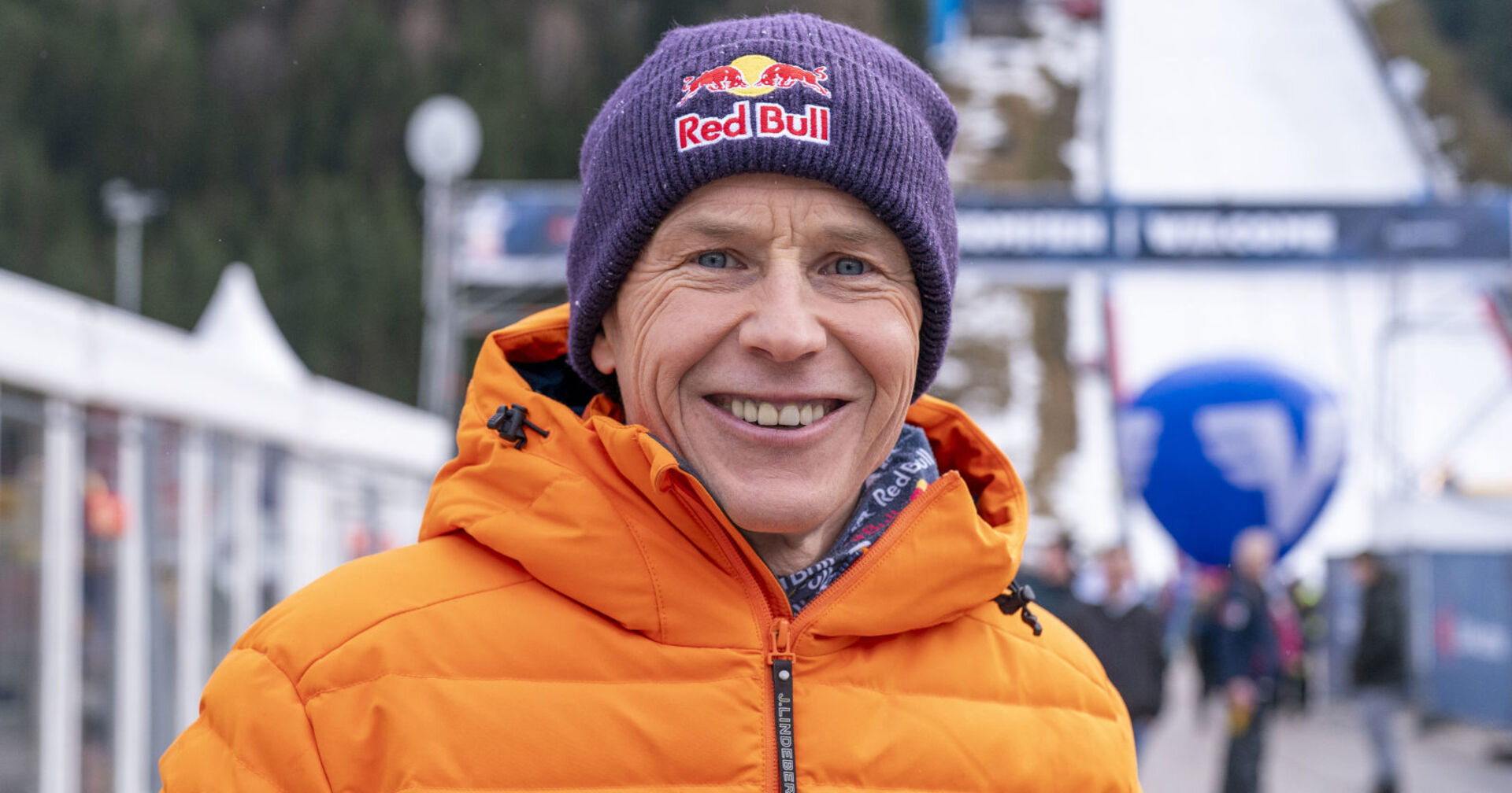 Ein Mann in oranger Skijacke und mit "Red Bull"-Haube steht vor einer Skipiste