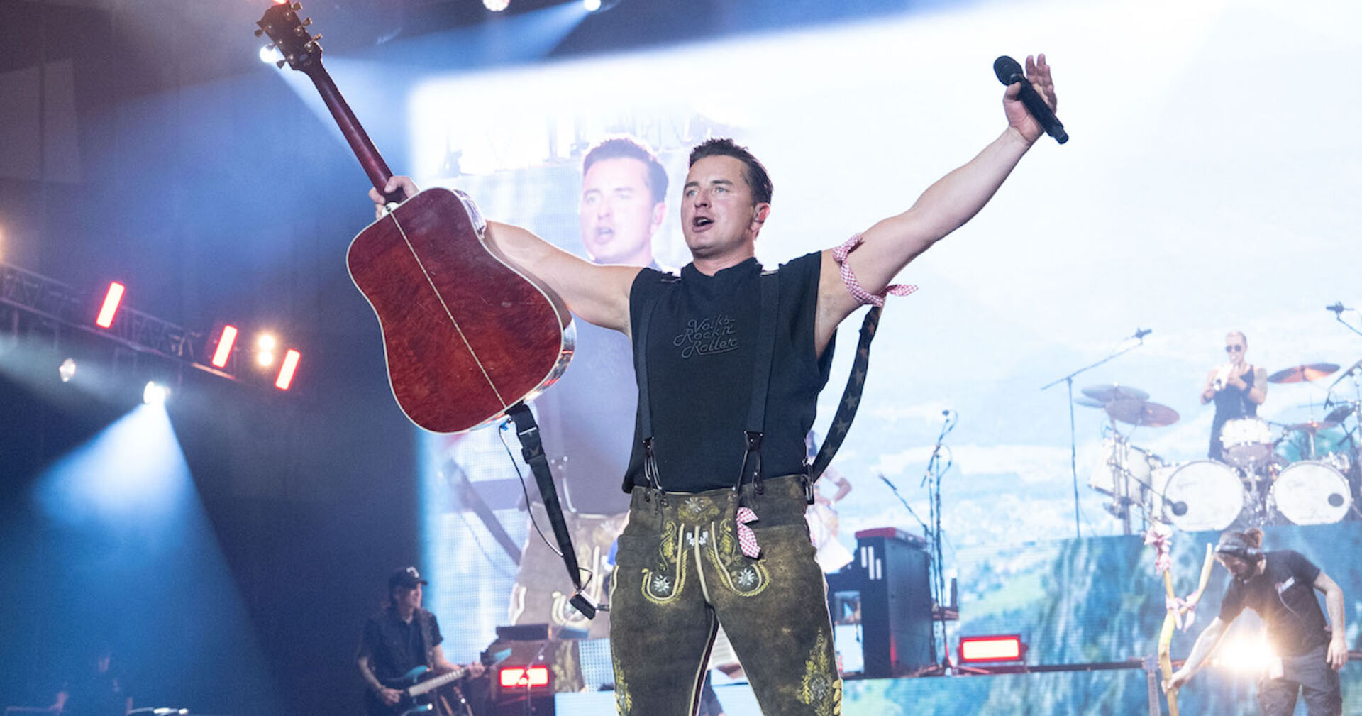Andreas Gabalier auf der Bühne mit einer Lederhose und einer Gitarre.