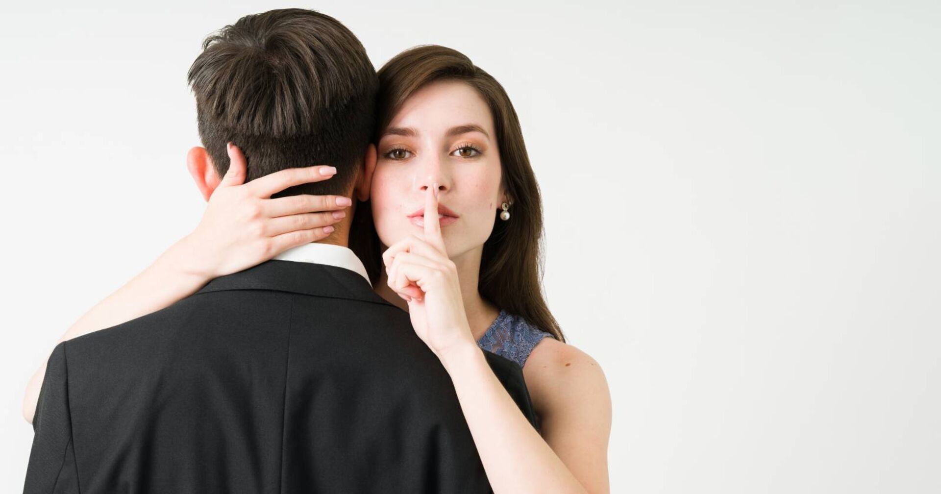 Junge Frau, die ihre Hand um den Nacken ihrer Affäre gelegt hat, der mit dem Rücken zur Kamera steht. Sie hat den ausgestreckten Zeigefinger auf die Lippen gelegt, um ein "Geheimnis" zu symbolisieren