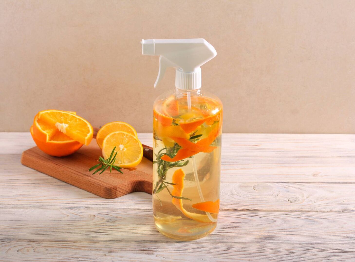 Sprühflasche mit Essig, Orangenschalen und Rosmarinzweigen. Im Hintergrund ist ein Holzbrett mit einer aufgeschnittenen Orange zu sehen.
