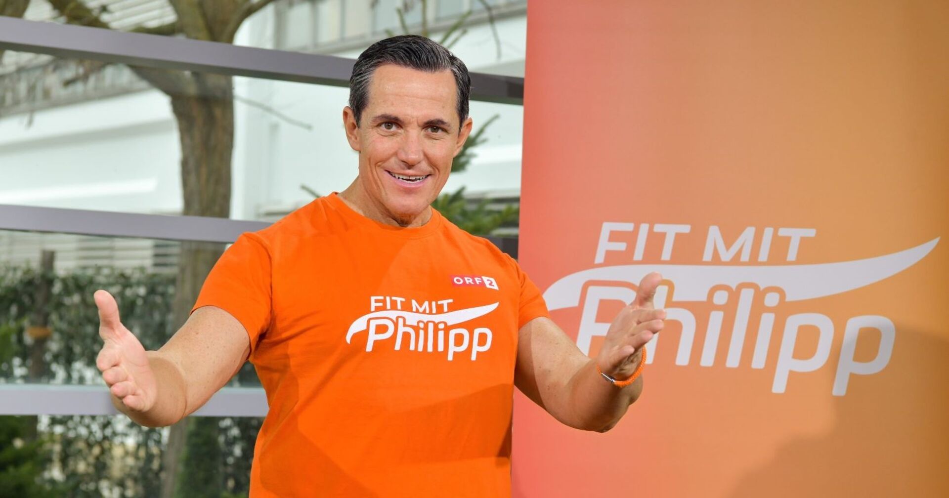 Philipp Jelinek in seine Fitness-Dress vor einem Banner mit der Aufschrift "Fit mit Philipp"