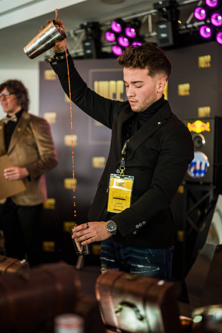 Junger Barkeeper, der gerade sehr konzentriert einen Drink mixt.