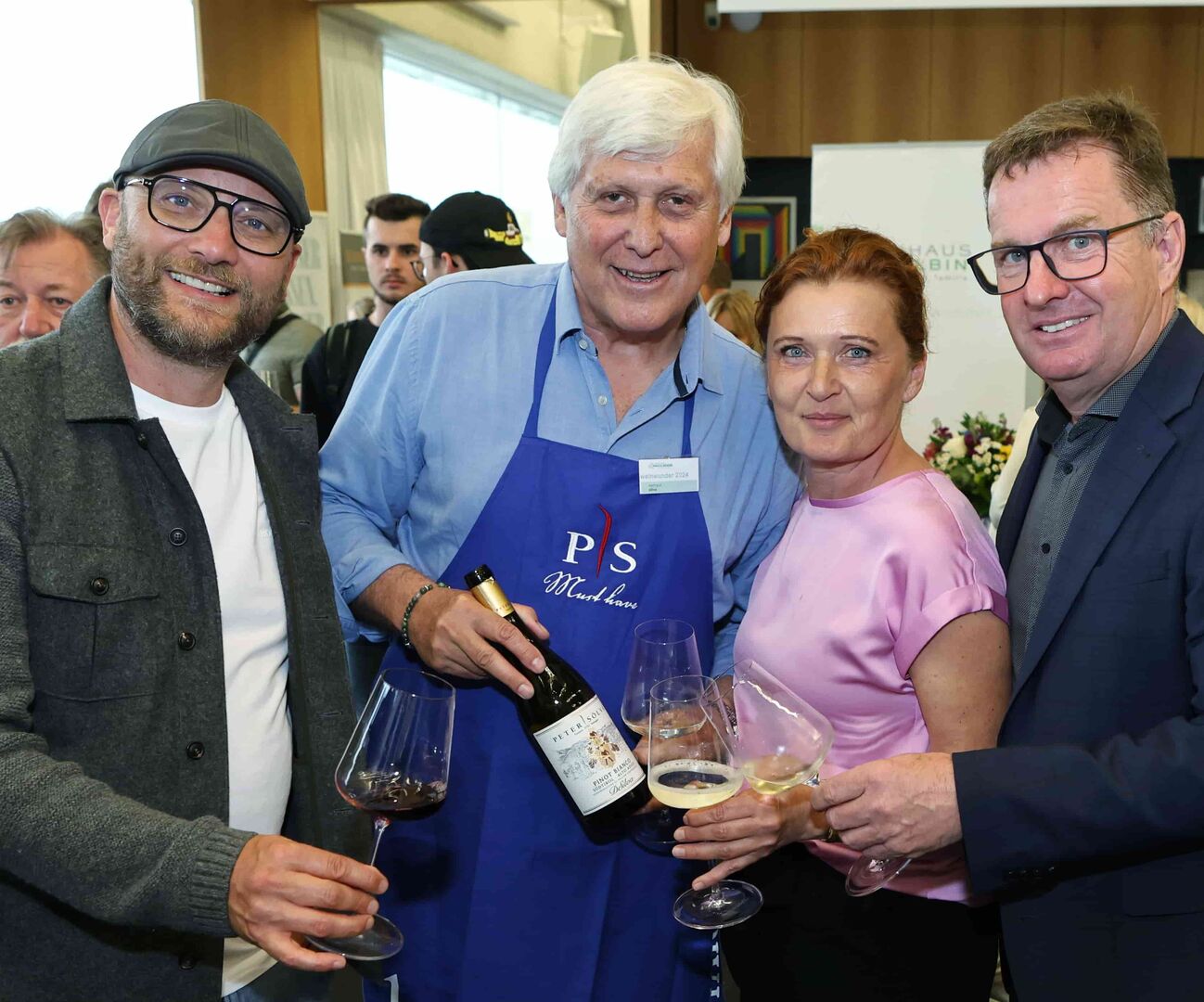 Von links nach recht: Ein Herr mit Bart, Brille und Kapperl hält ein Glas Rotwein, daneben ein Mann mit weißen Haaren und blauer Schürze und einer Flasche Wein, links von ihm eine Frau mit rötlichem Haar und pinker Bluse mit einem Glas Weißwein und ein Herr mit blauem Sakko, brauner Brille. Auch er hält ein Glas Weißwein.