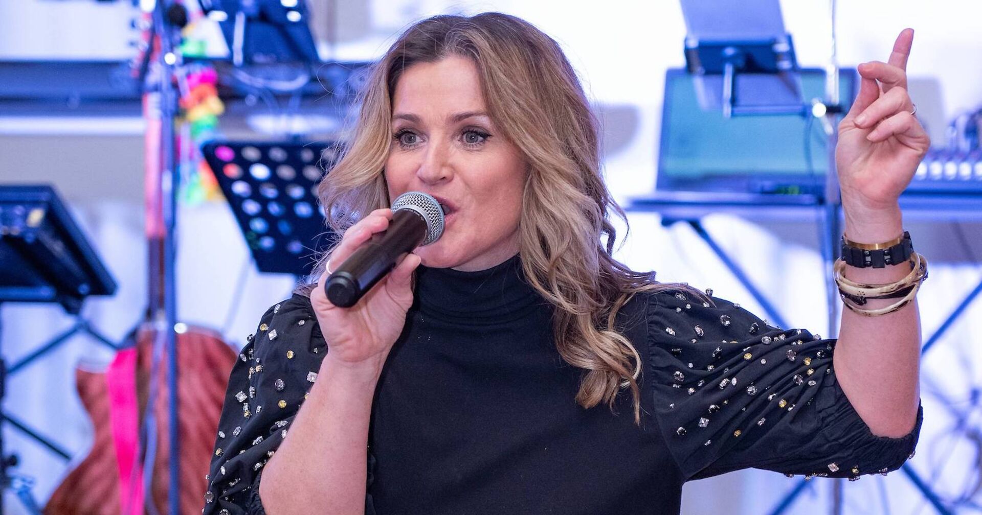 Lizz Görgl mit einem schwarzen Oberteil und einem Mikrofon auf einer Bühne. Ihre Haare sind offen und gewellt.