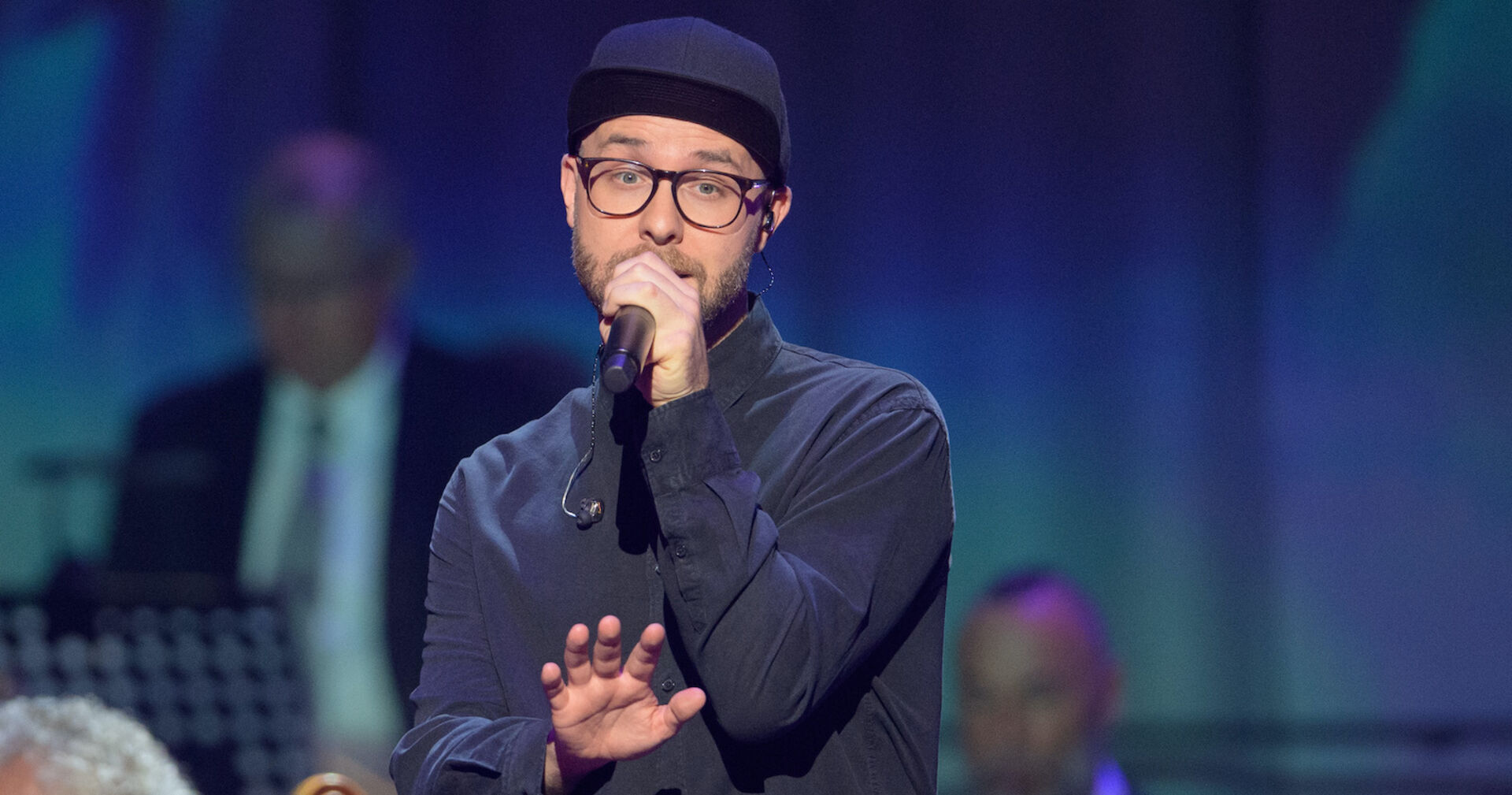 Mark Forster auf der Bühne mit einem Mikrofon und einer Kappe.