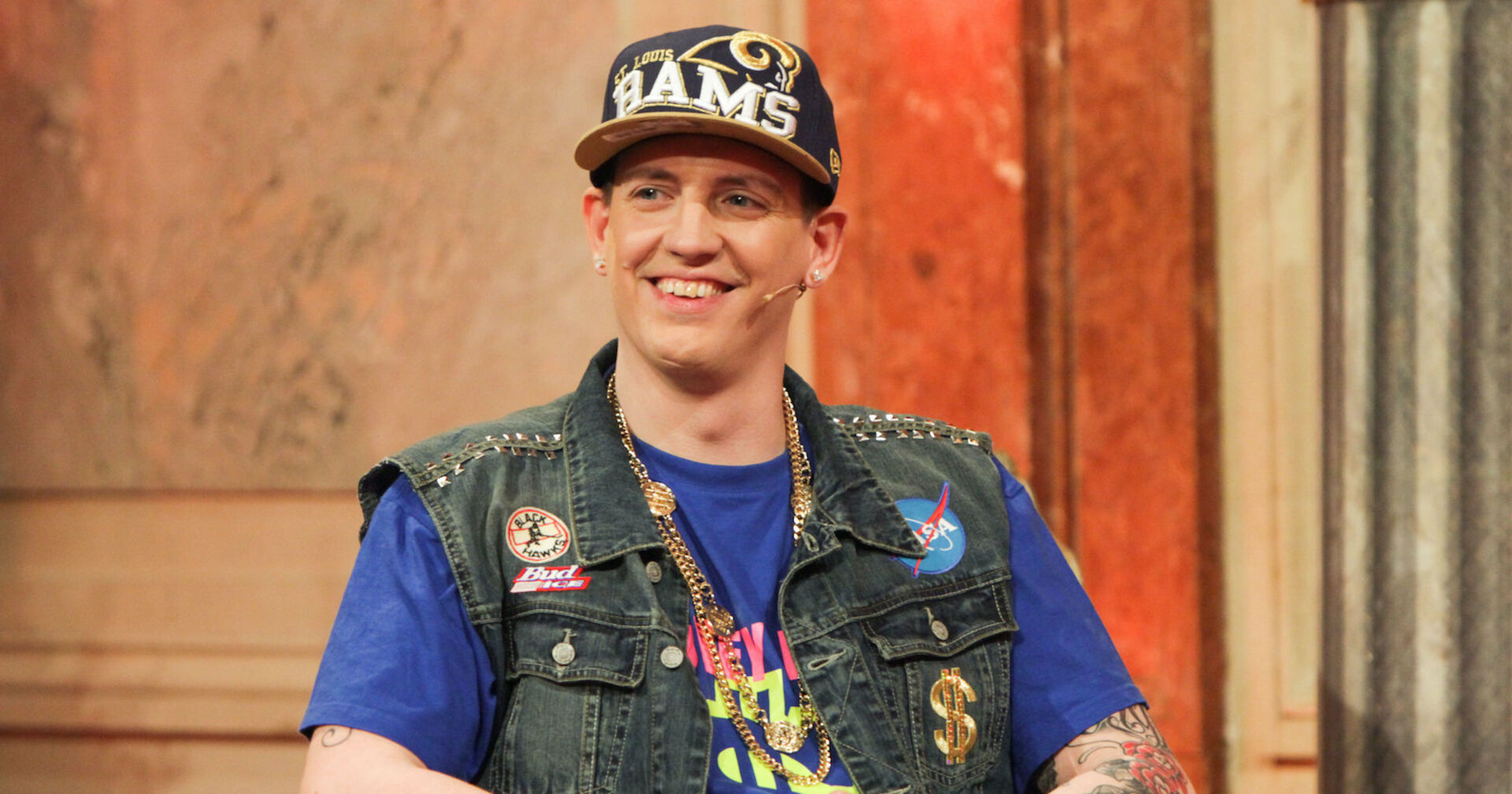 Money Boy mit einer großen Kappe und einer Jacke mit Sticker bei "Wir sind Kaiser".
