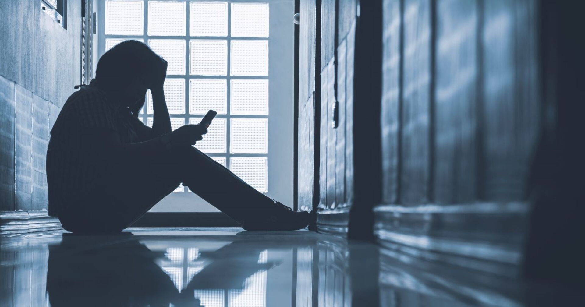 Eine Schülerin sitzt im Gang und starrt auf ihre Handy.