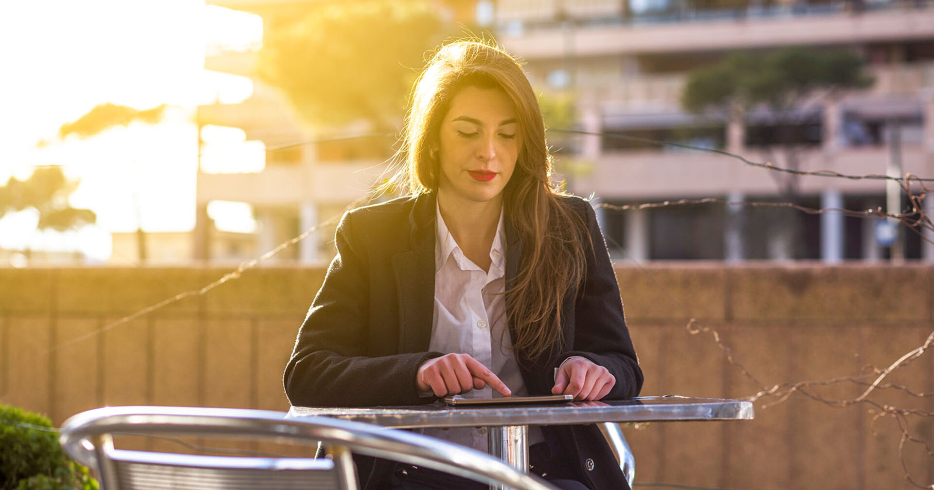 Frau die in einem Garten sitzt und auf ihrem Smartphone tippt