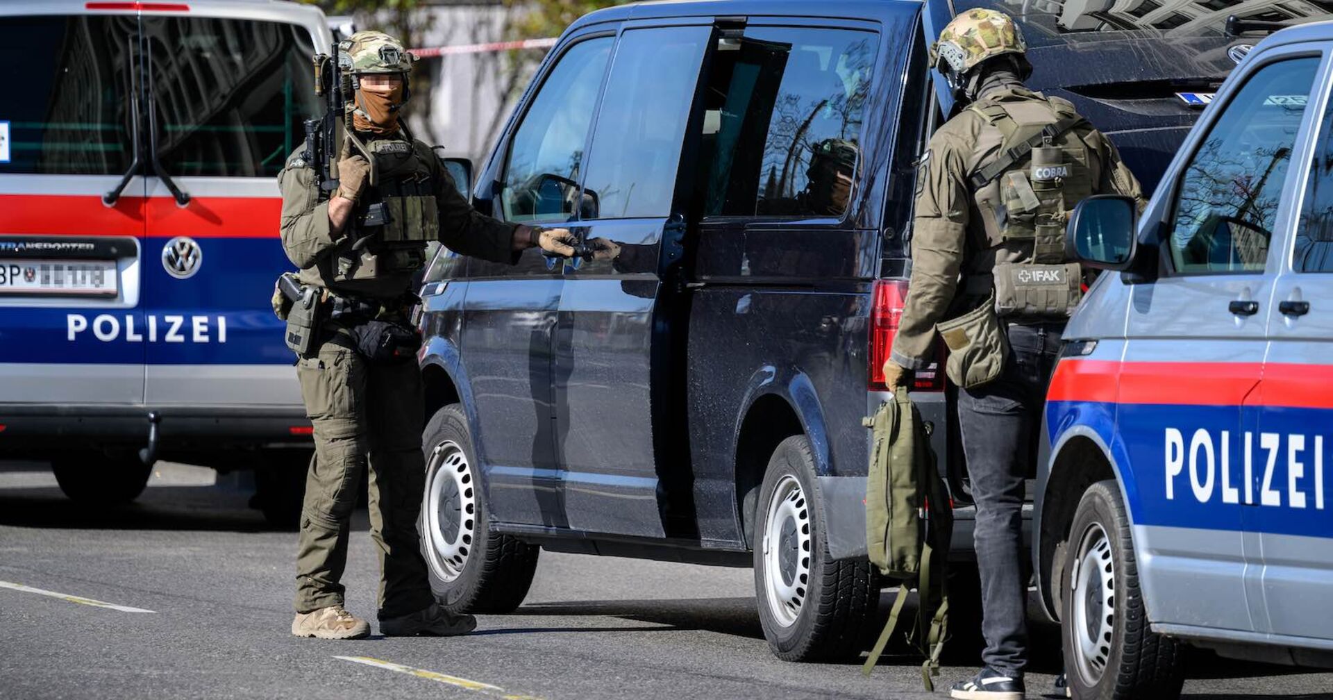 Zwei Cobra-Einsatzkräfte vor Polizeiautos.