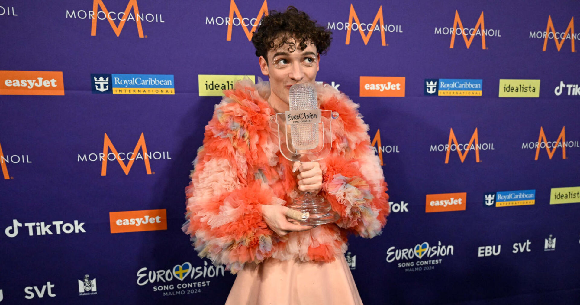 Mann in einer Plüsch-Jacke hält eine gläserne Trophäe in der Hand