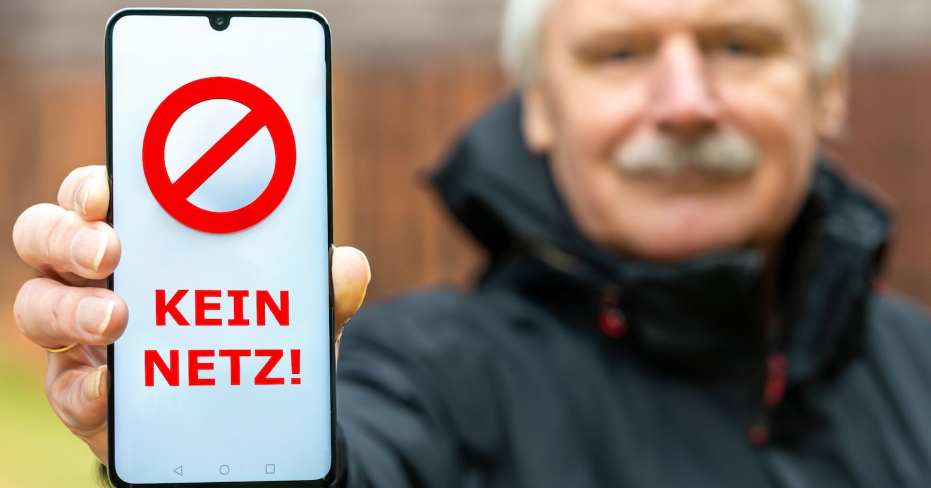 Eine Mann hält eine Handy mit einer "Kein Netz"-Aufschrift in die Kamera.