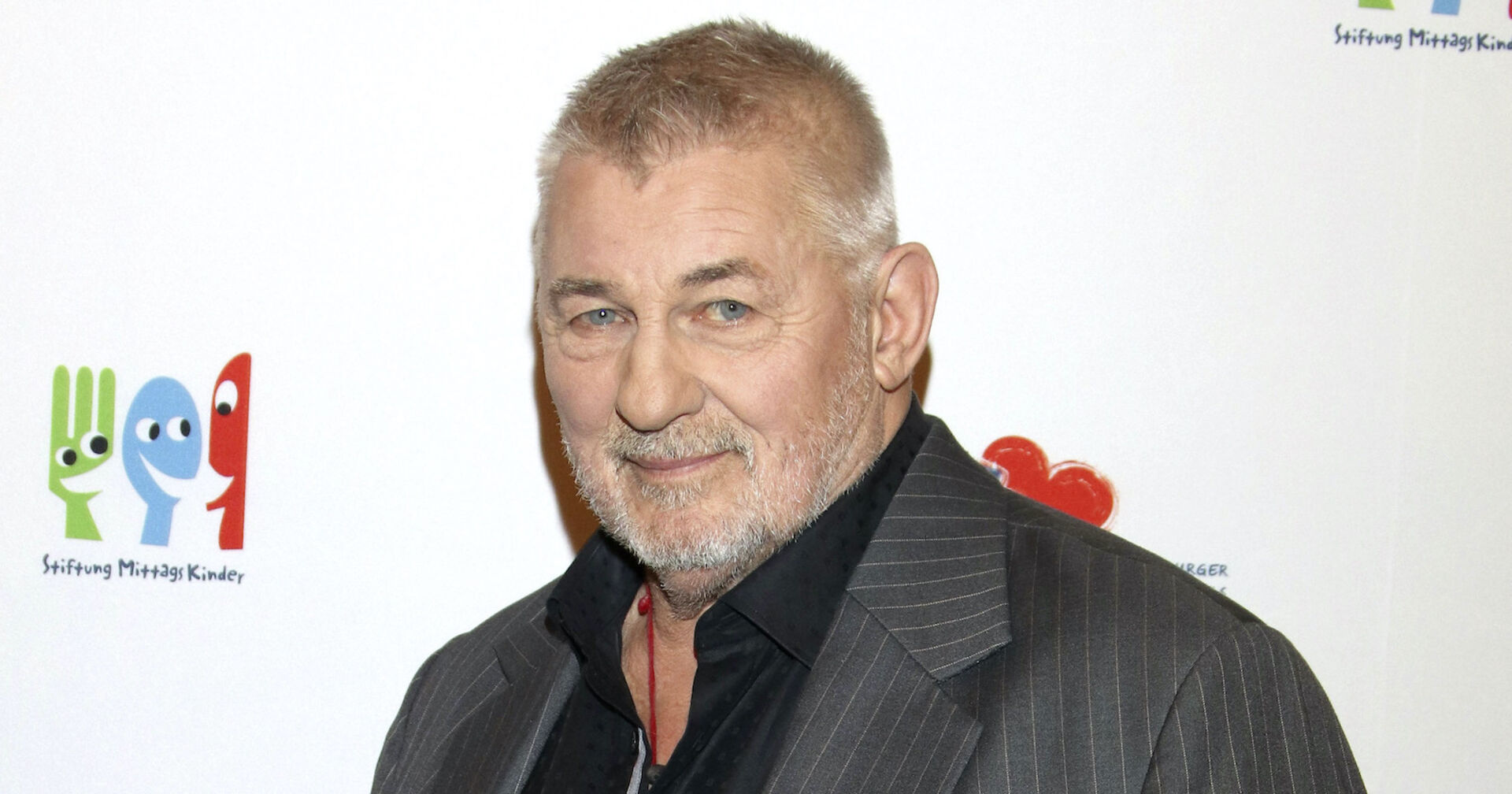 Heinz Hoenig mit einem grauen Anzug und einem schwarzen Hemd bei einem Event.