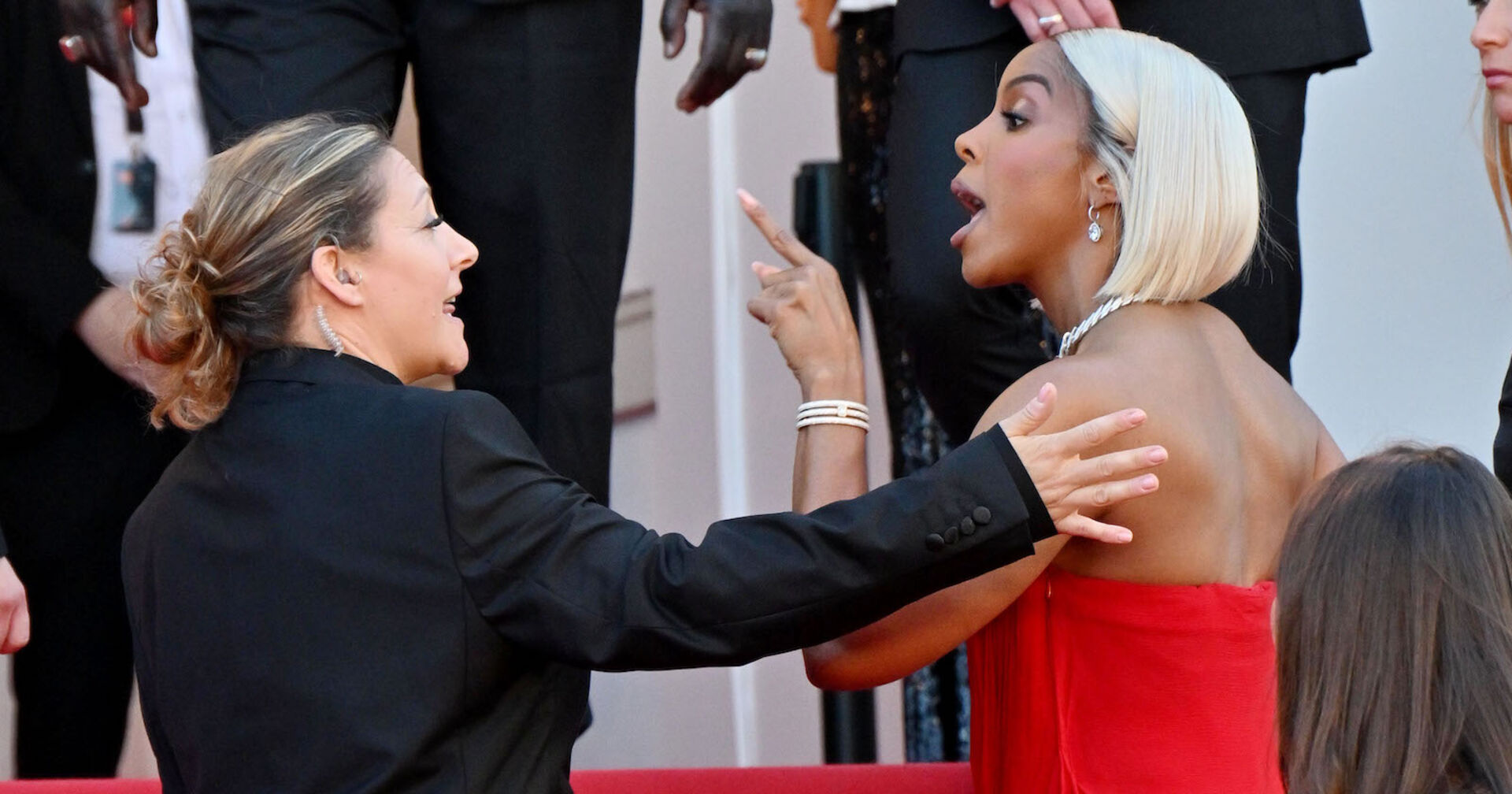 Kelly Rowland auf dem roten Teppich. Sie trägt blonde Haare und ein rotes Kleid und streitet mit dem sicherheitspersonal.