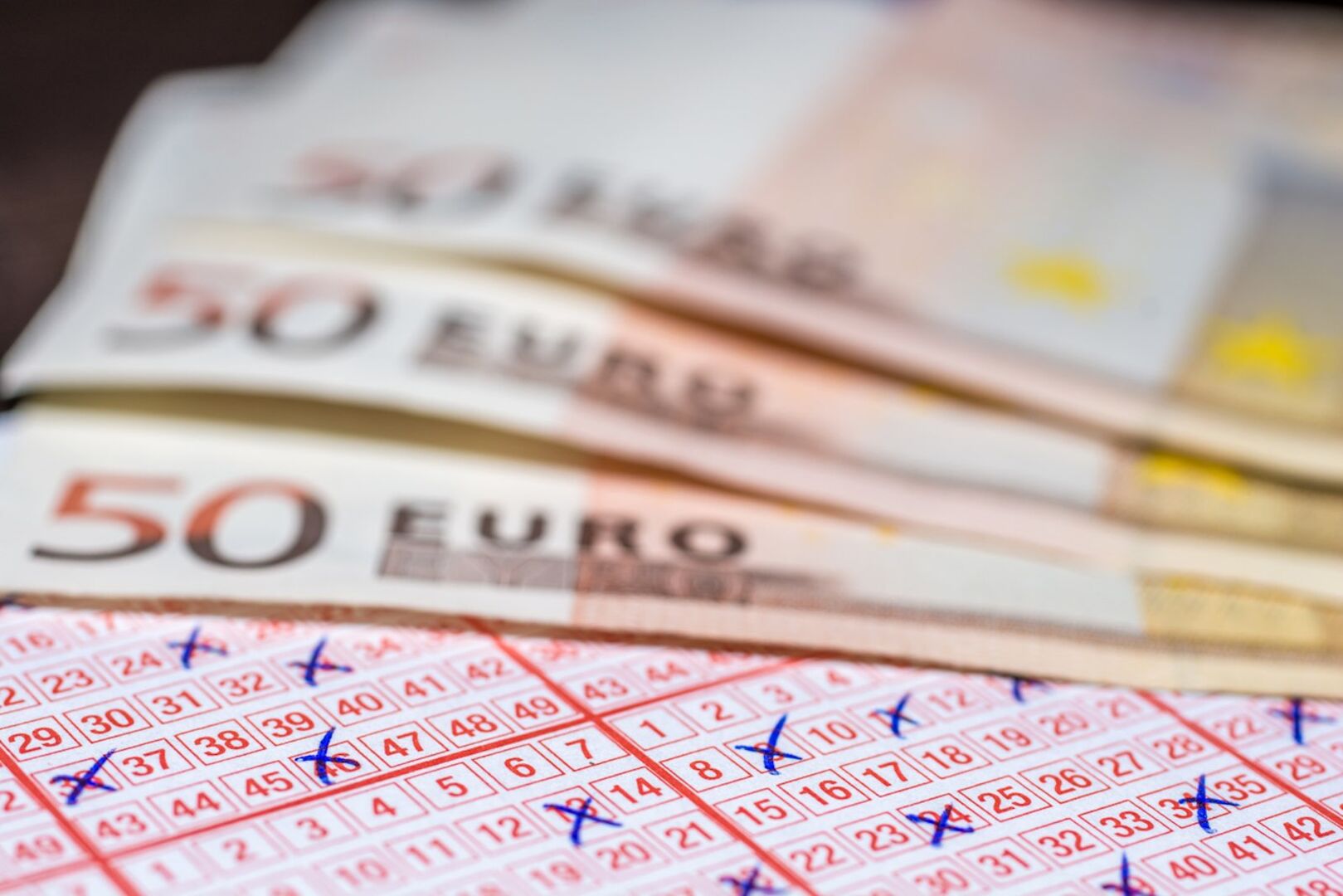 Lottoschein mit angekreuzten Zahlen, Geld im Hintergrund.