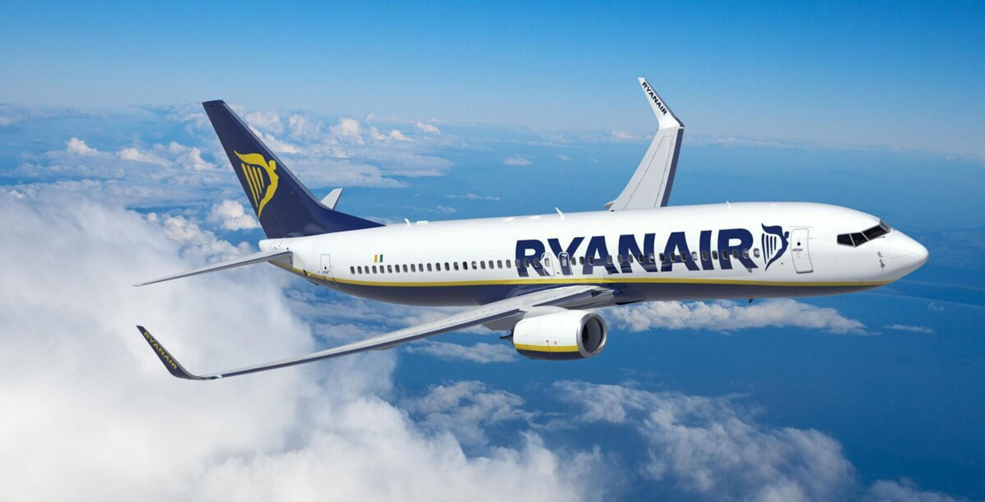 Ein weißes Flugzeug mit der blauen Aufschrift Ryanair schwebt über weißen Wolken und dem blauen Himmel.