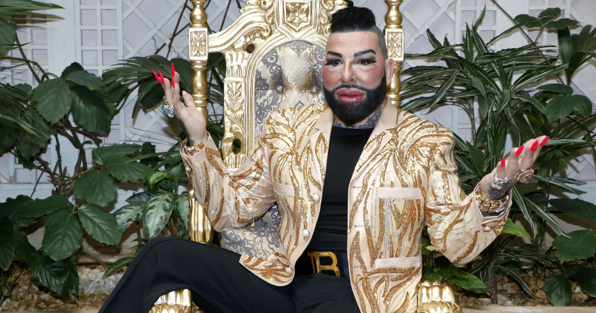 Harald Glööckler mit einer goldenen Jacke auf einem goldenen Stuhl.