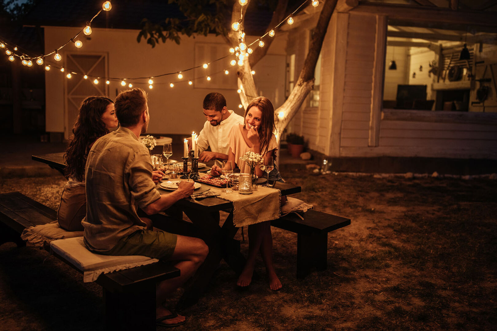 Freunde sitzen unter einer Lichterkette | Credit: iStock.com/bernardbodo