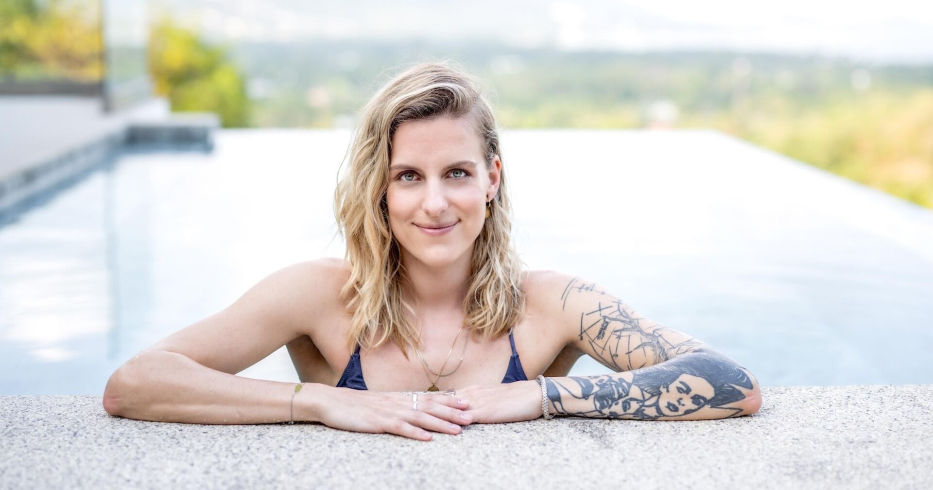 Die neue Princess Charming mit offenen blonden Haaren und einem Tattoo am Arm im Pool.