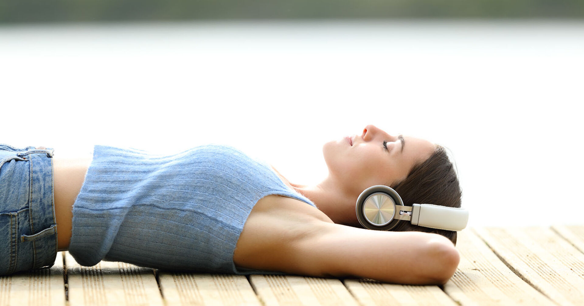 Frau liegt mit Kopfhörern auf einem Steg | Credit: iStock.com/Pheelings Media