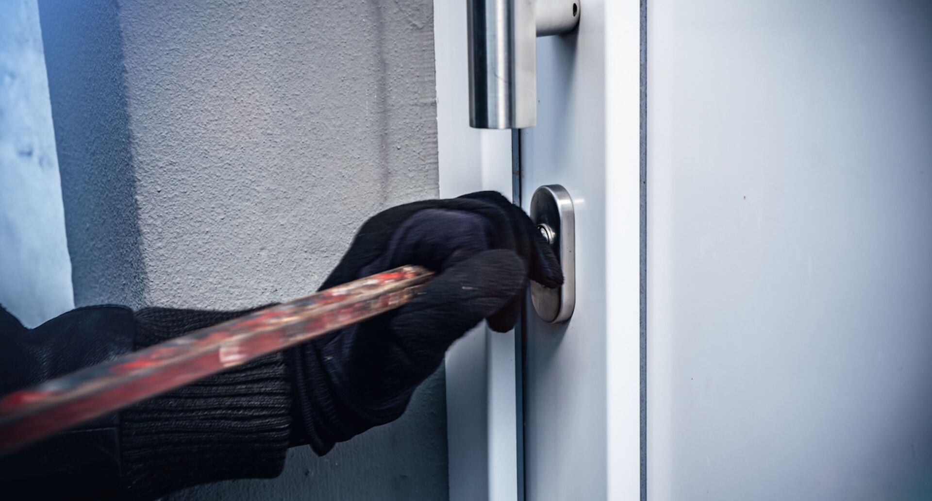 Einbrecher mit schwarzen Handschuhen bricht Tür auf
