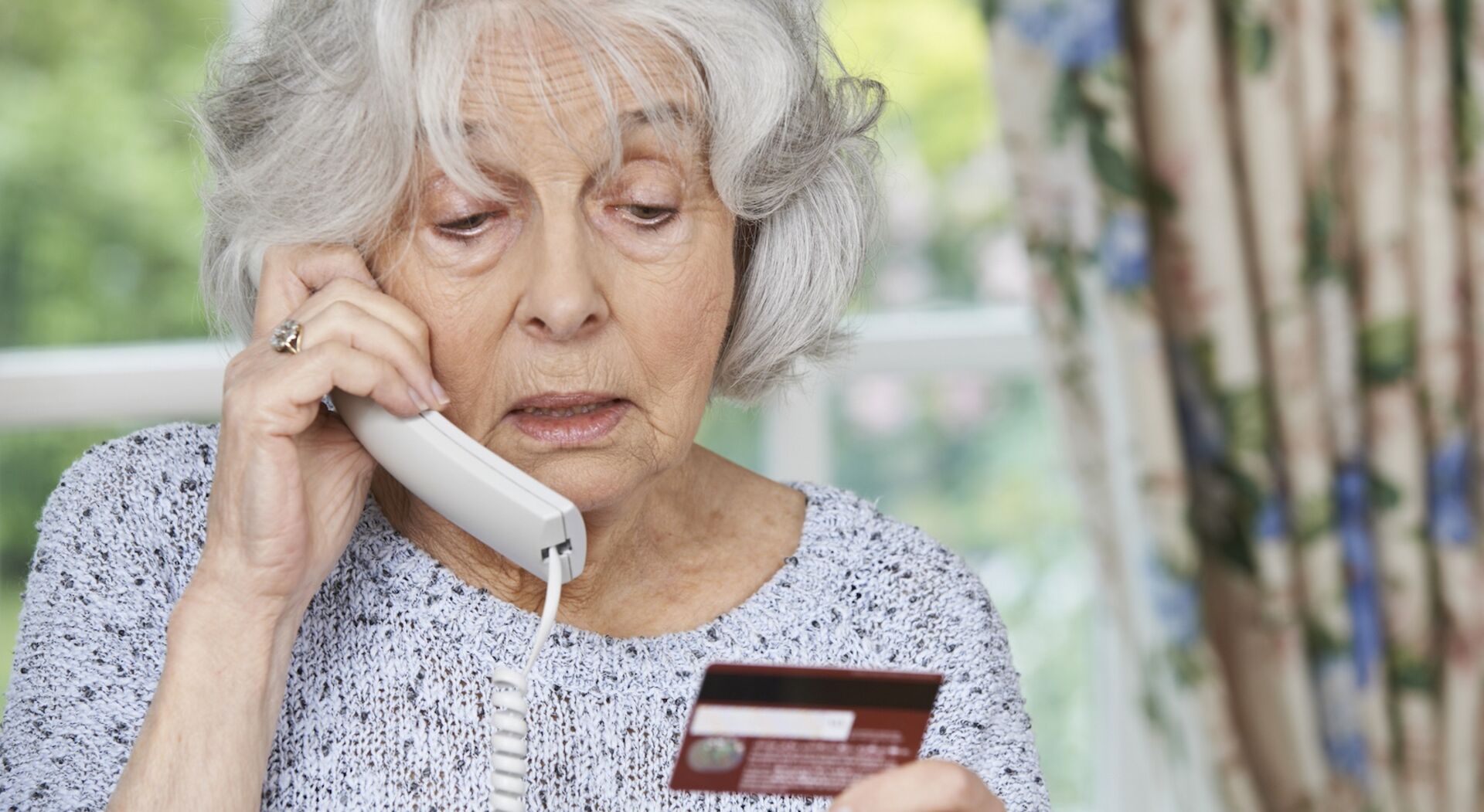 ältere Dame telefoniert und wirft dabei einen Blick auf ihre Kreditkarte