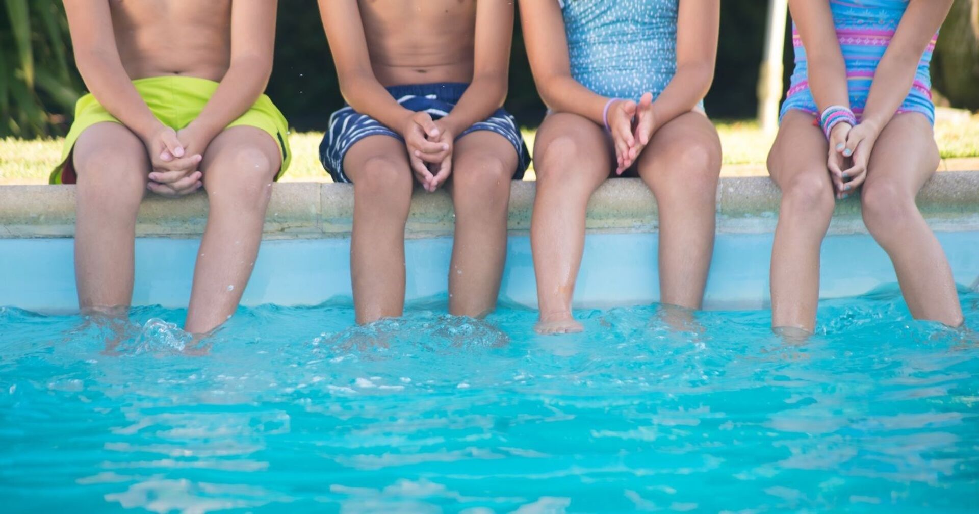 Vier Kinder sitzen am Beckenrand eines Schwimmbads.