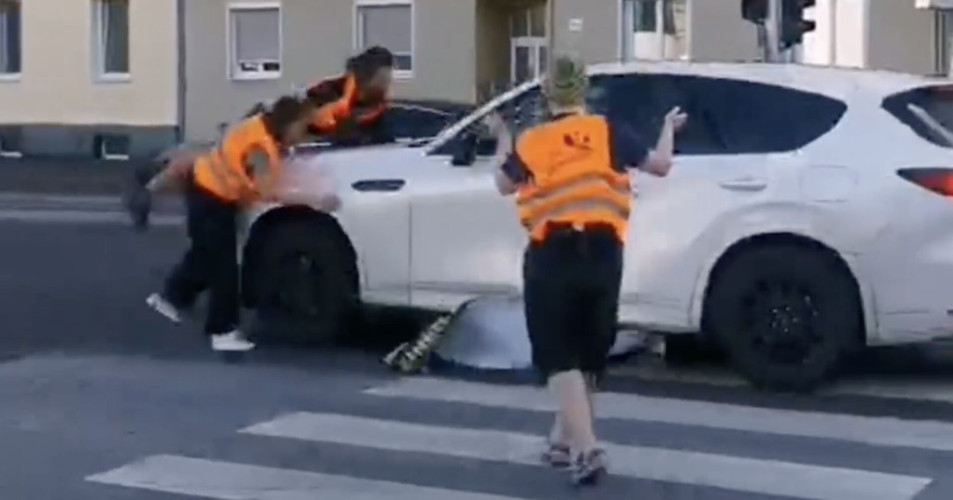 Ein weißes Auto fährt Klimaaktivisten auf der Straße nieder.
