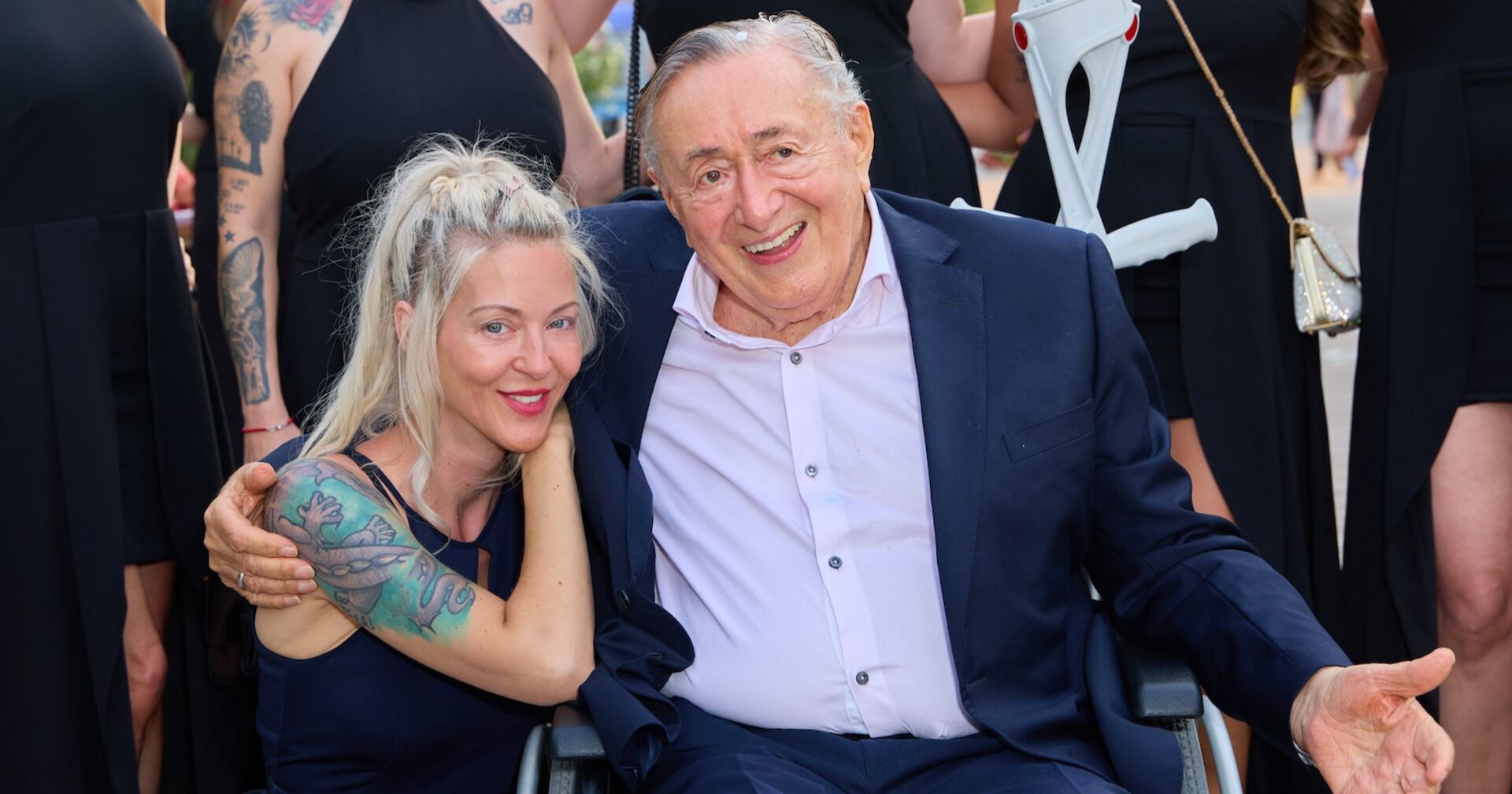 Richard und Simone Lugner bei einem Fest. Richard Lugner sitzt im Rollstuhl.