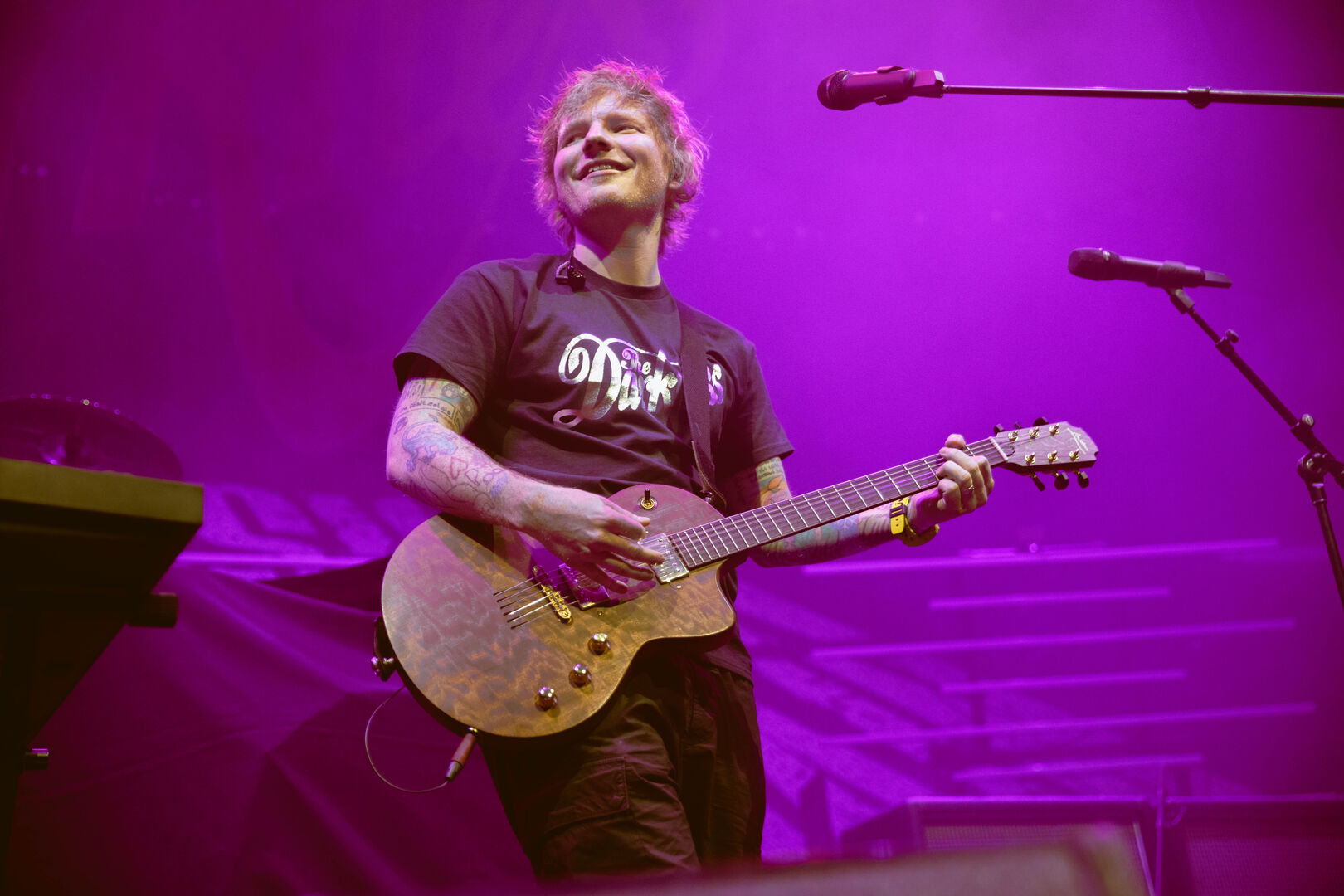 Ed Sheeran, der auf einer in violettes Licht getauchten Bühne Gitarre spielt