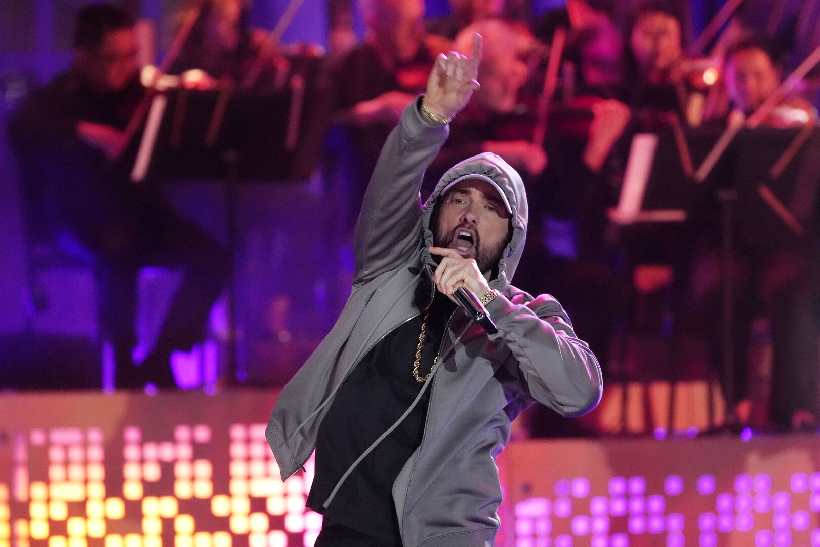Der Rapper Eminem singt vor einem Orchester auf einer Bühne in ein Mikrophon