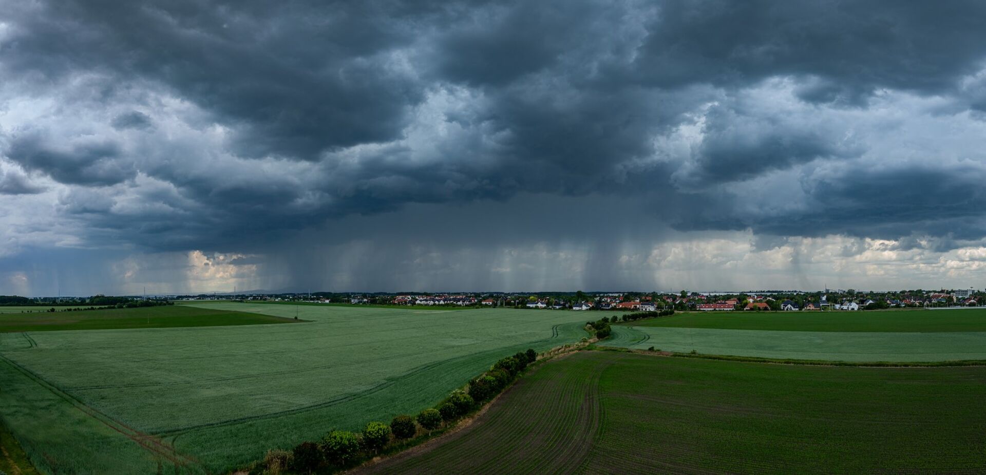 Gewitter mit Starkregen über einem grünen Feld.