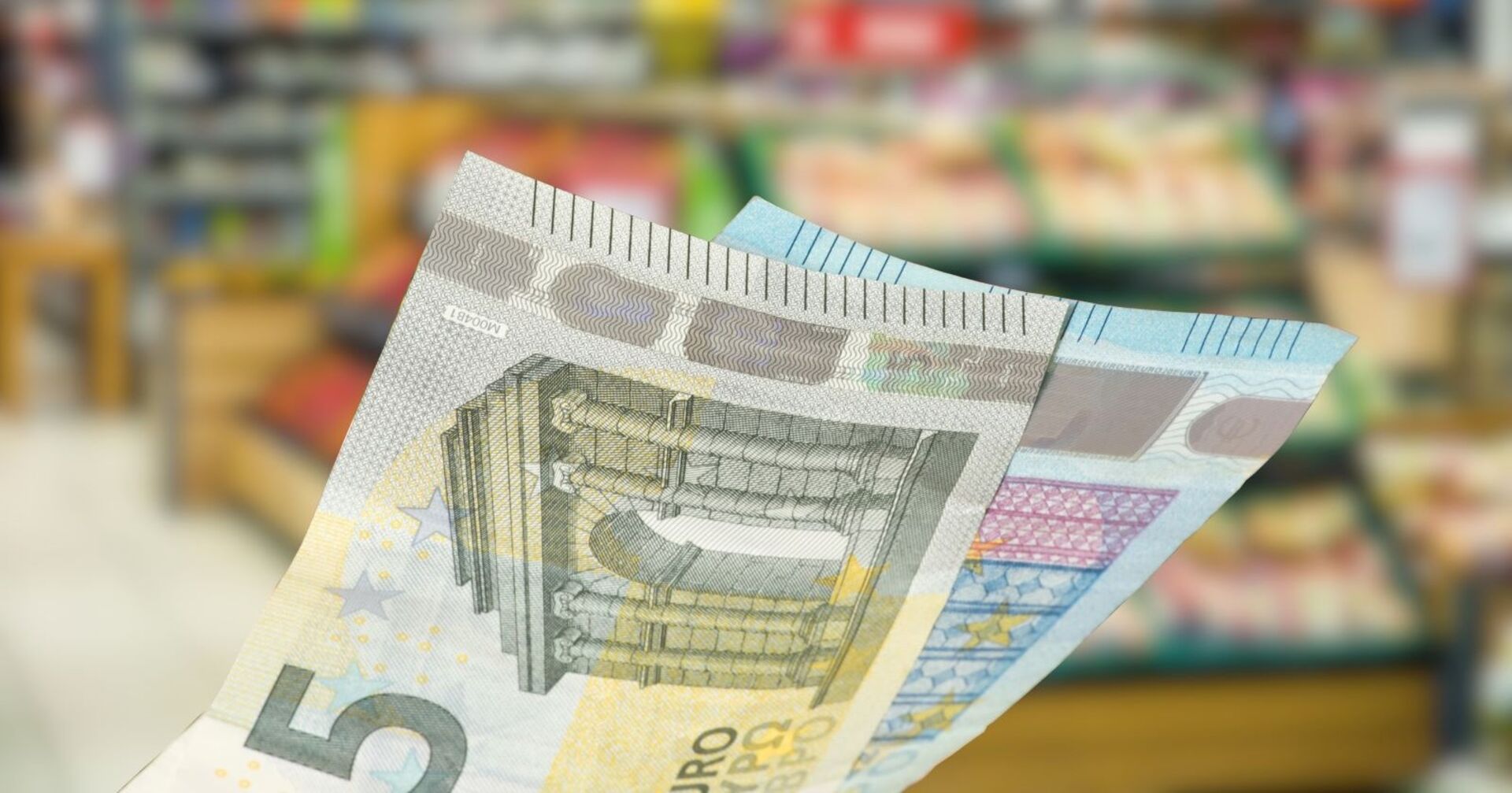 25 Euro in Scheinen vor dem Hintergrund eines Supermarkts.