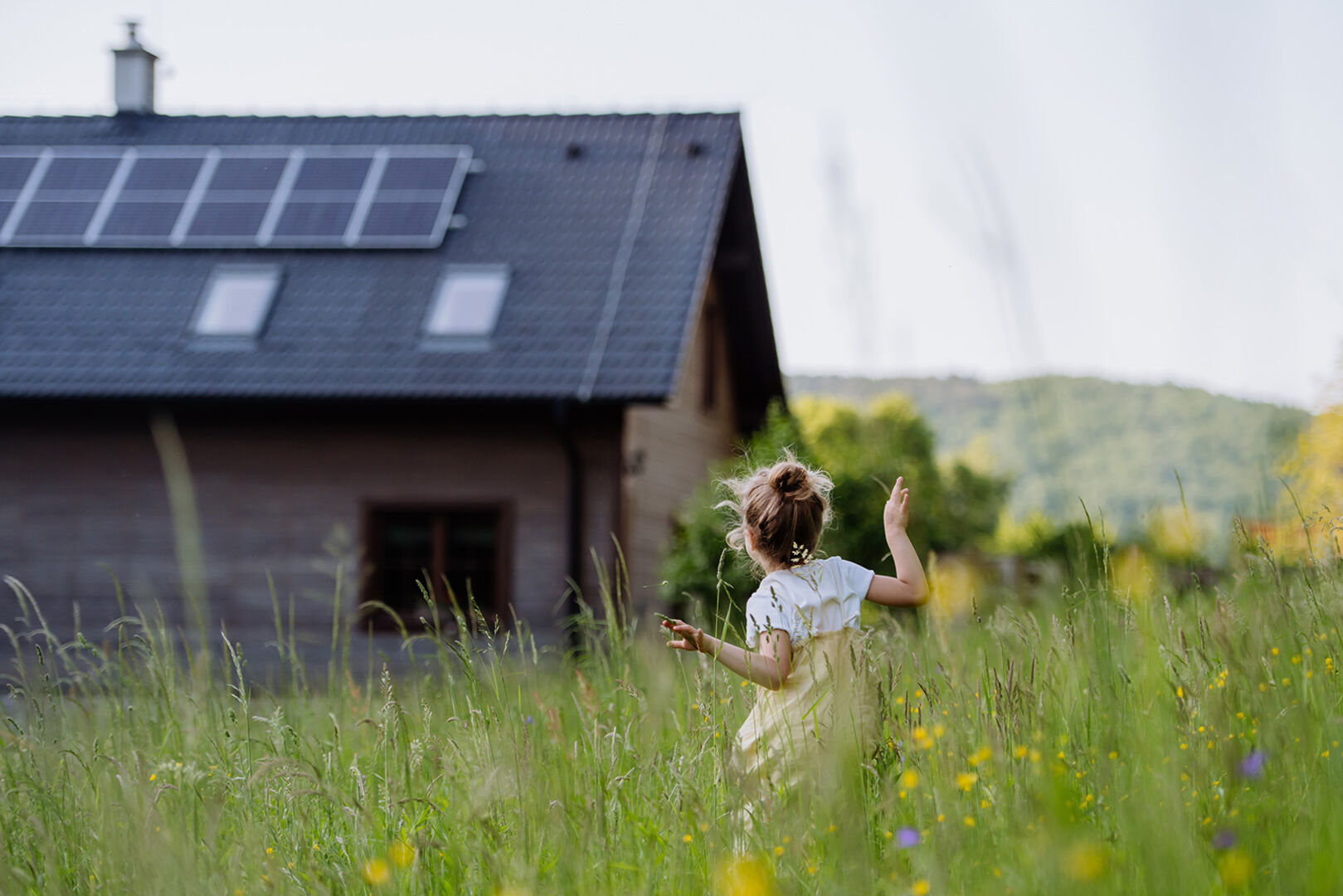 Kleines Mädchen tollt durch die Wiese vor dem Haus ihrer Eltern | Credit: iStock.com/Halfpoint